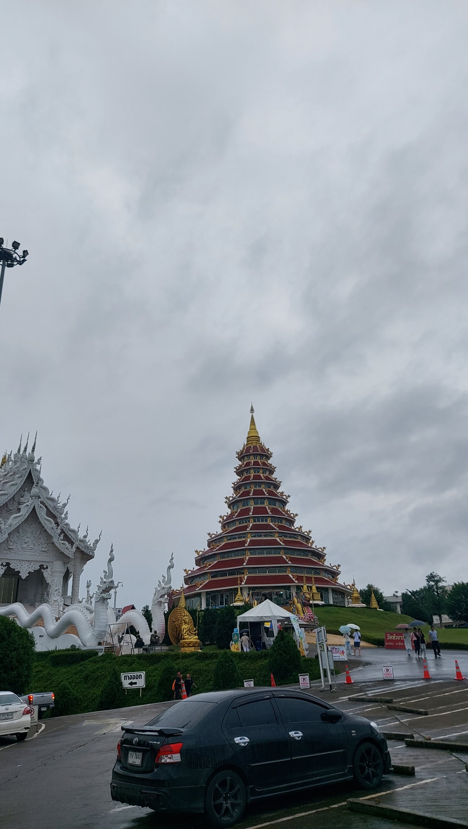 Fachada externa e grandiosa da torre pagoda com telhados vermelhos, detalhes dourados e estátuas sob um céu nublado em Chiang Rai.