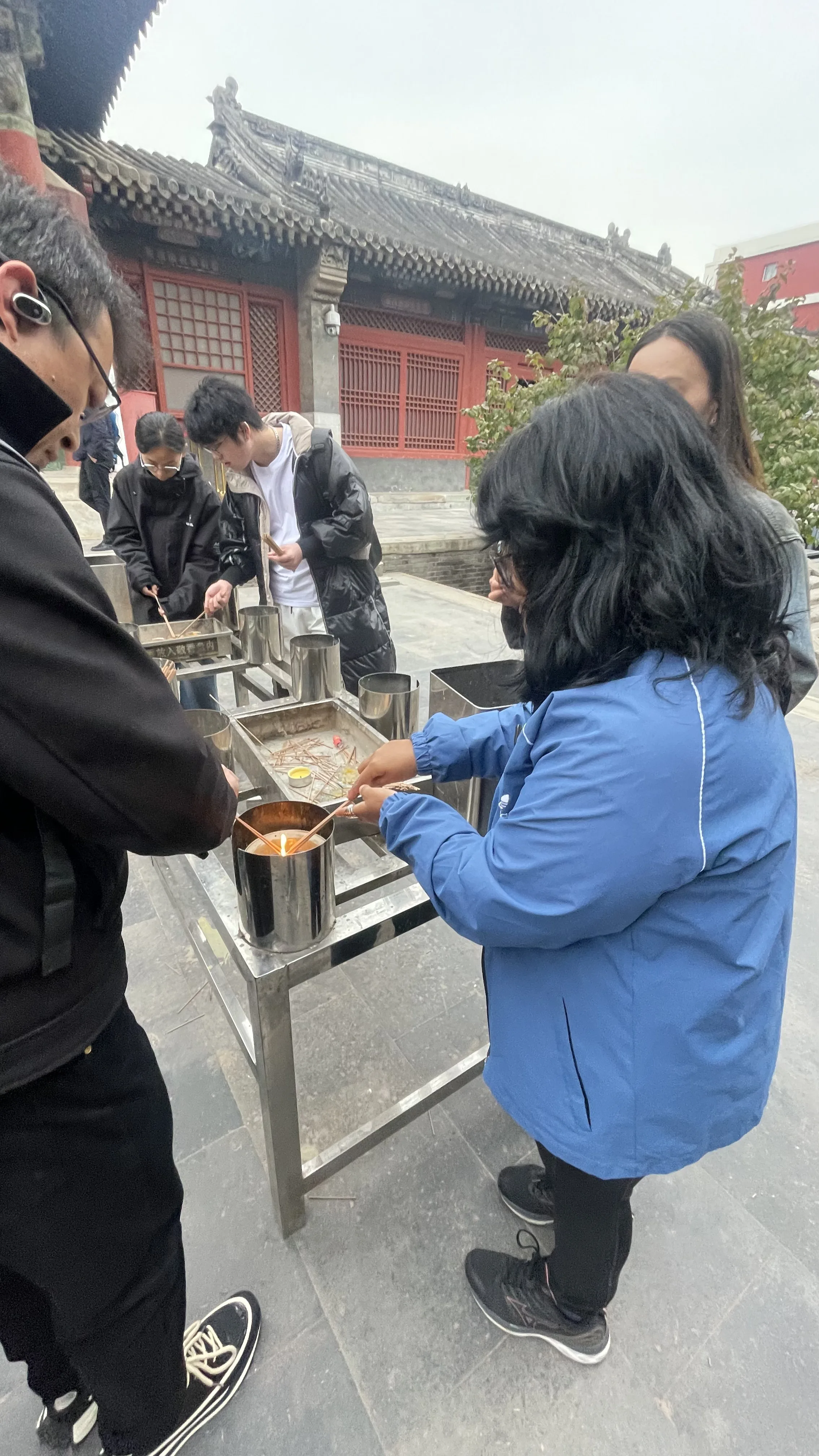 Mulher de casaco azul acende incensos em recipiente de metal em pátio de templo em Pequim.