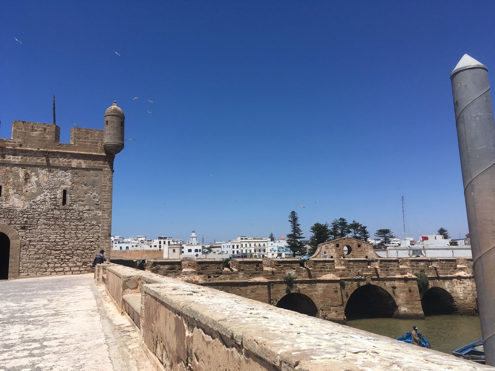 Ponte de pedra antiga e muralha de fortificação com torres em Essaouira, sob um céu azul limpo