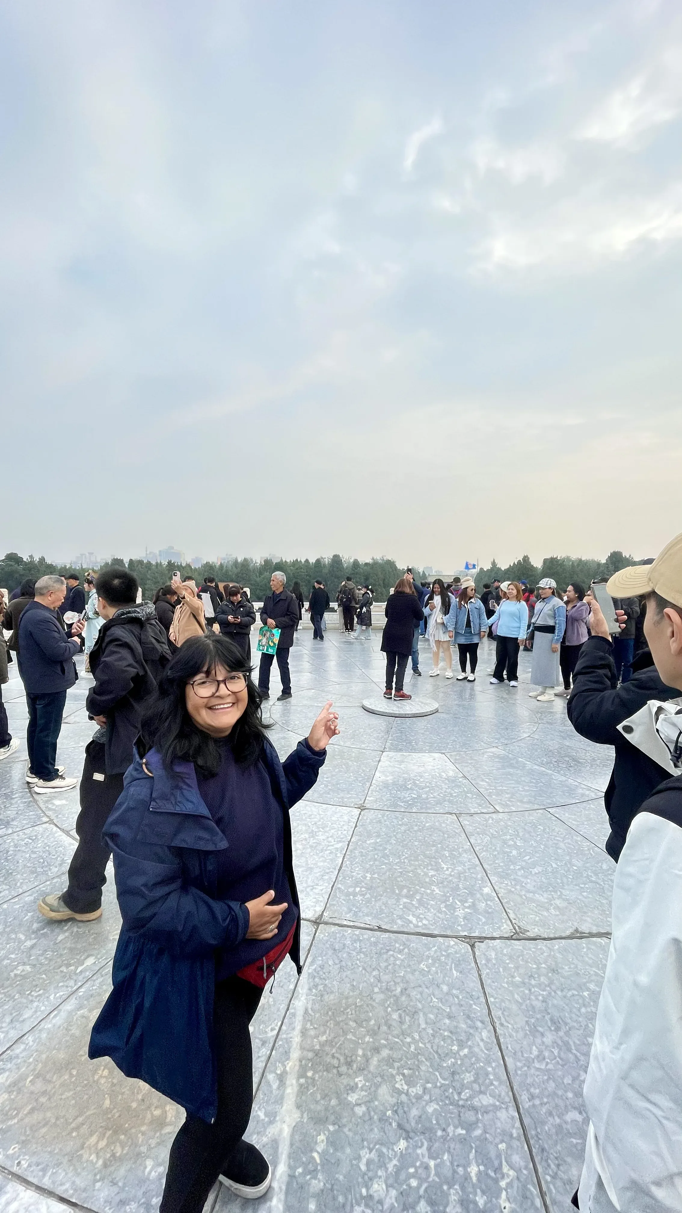 Mulher sorri e aponta para o centro da laje circular de pedra rodeada por turistas no Altar do Céu em Pequim.