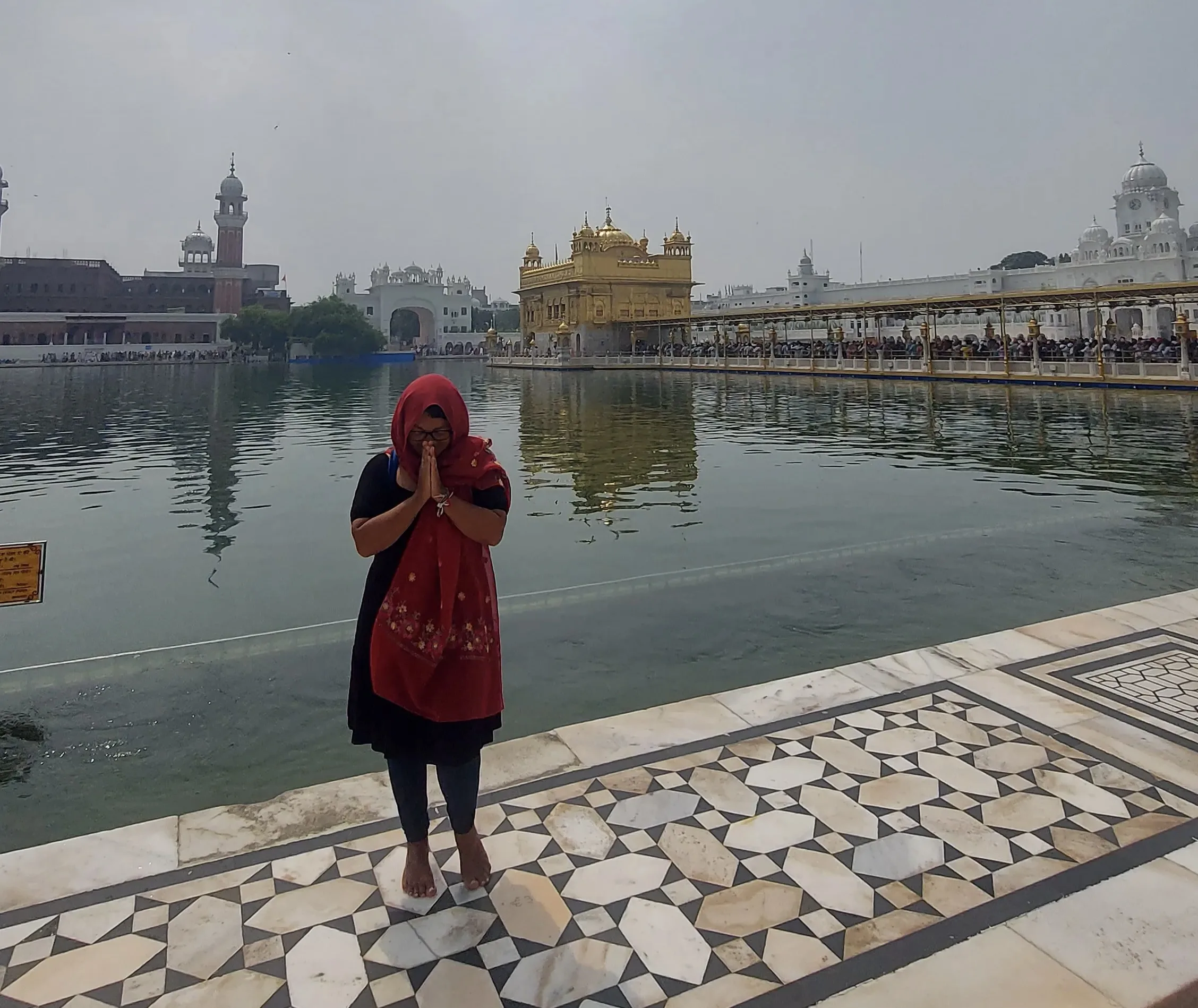 Viajante com a cabeça coberta por um lenço vermelho posando com as mãos juntas em sinal de agradecimento no pátio de mármore do Templo Dourado, em Amritsar, na Índia.