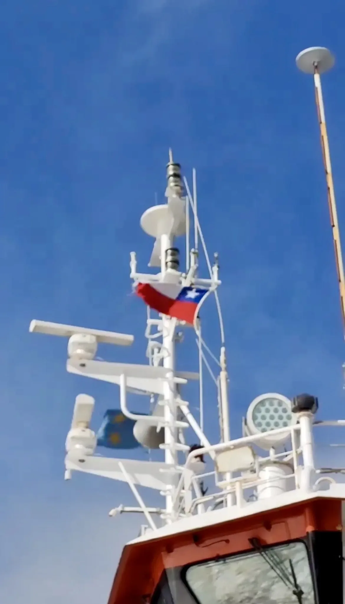 Bandeira do Chile tremulando no mastro de radar e antenas de comunicação de uma embarcação no Estreito de Magalhães.