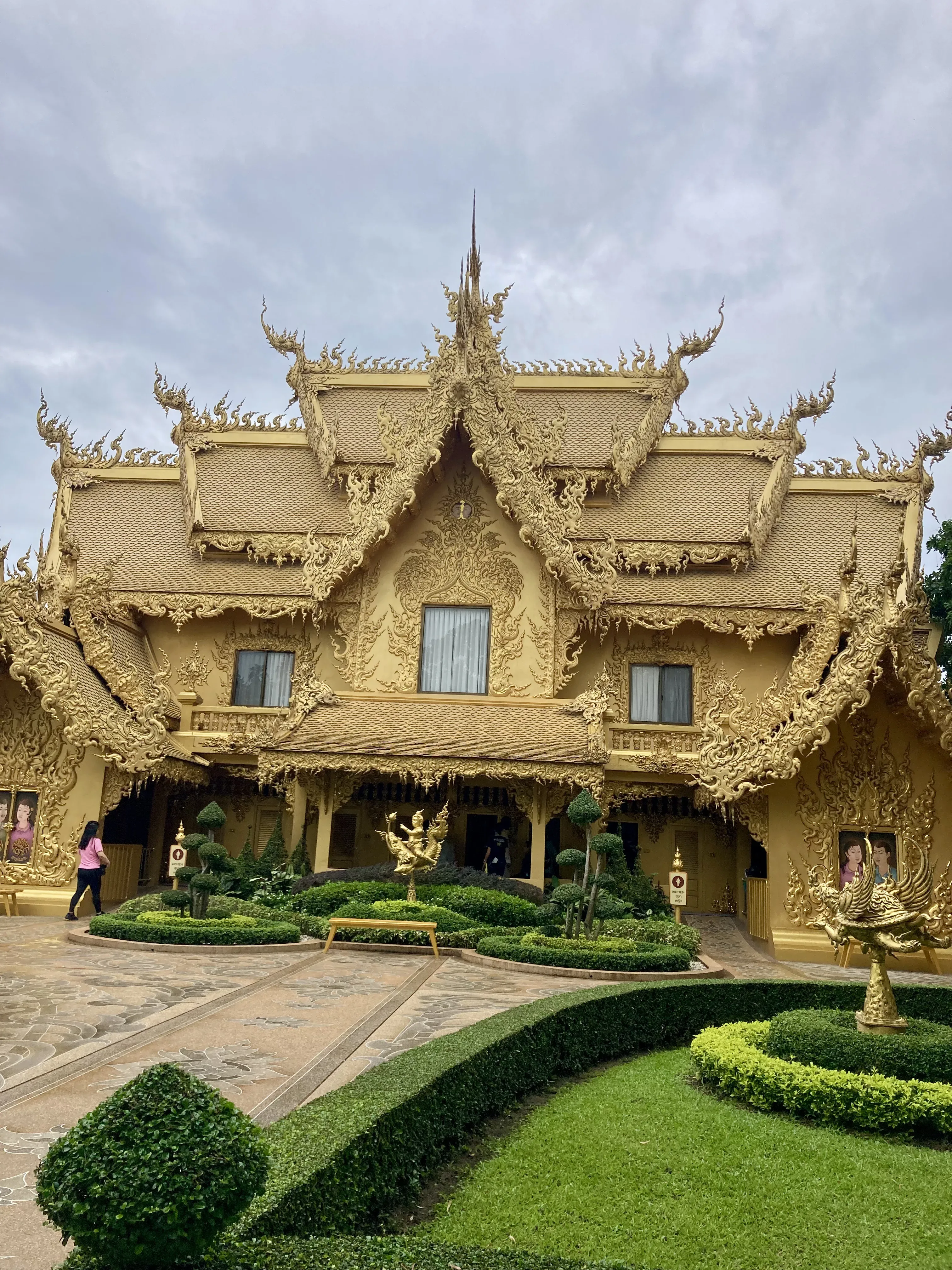 Fachada do impressionante edifício dourado dos banheiros públicos no complexo do Templo Branco em Chiang Rai, rodeado por jardins esculpidos.