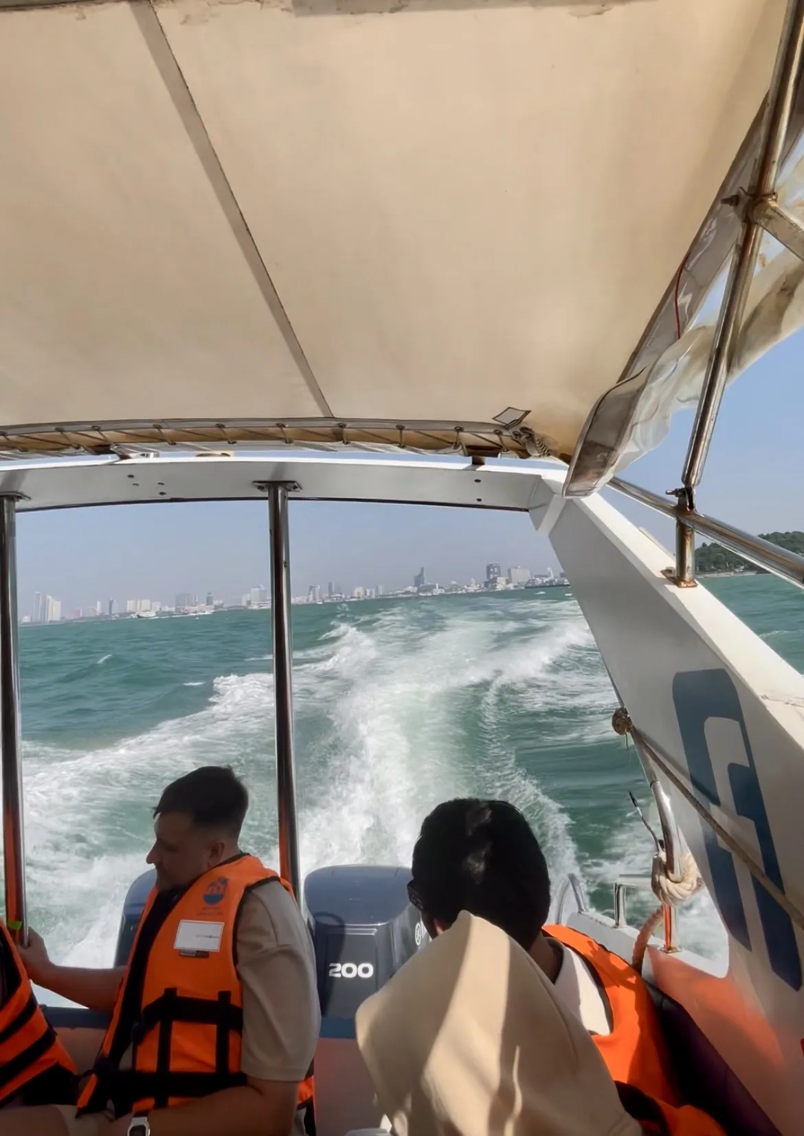 Passageiros com coletes salva-vidas a bordo de uma lancha rápida navegando em direção a Ko Lan, na Tailândia, com a silhueta da cidade ao fundo
