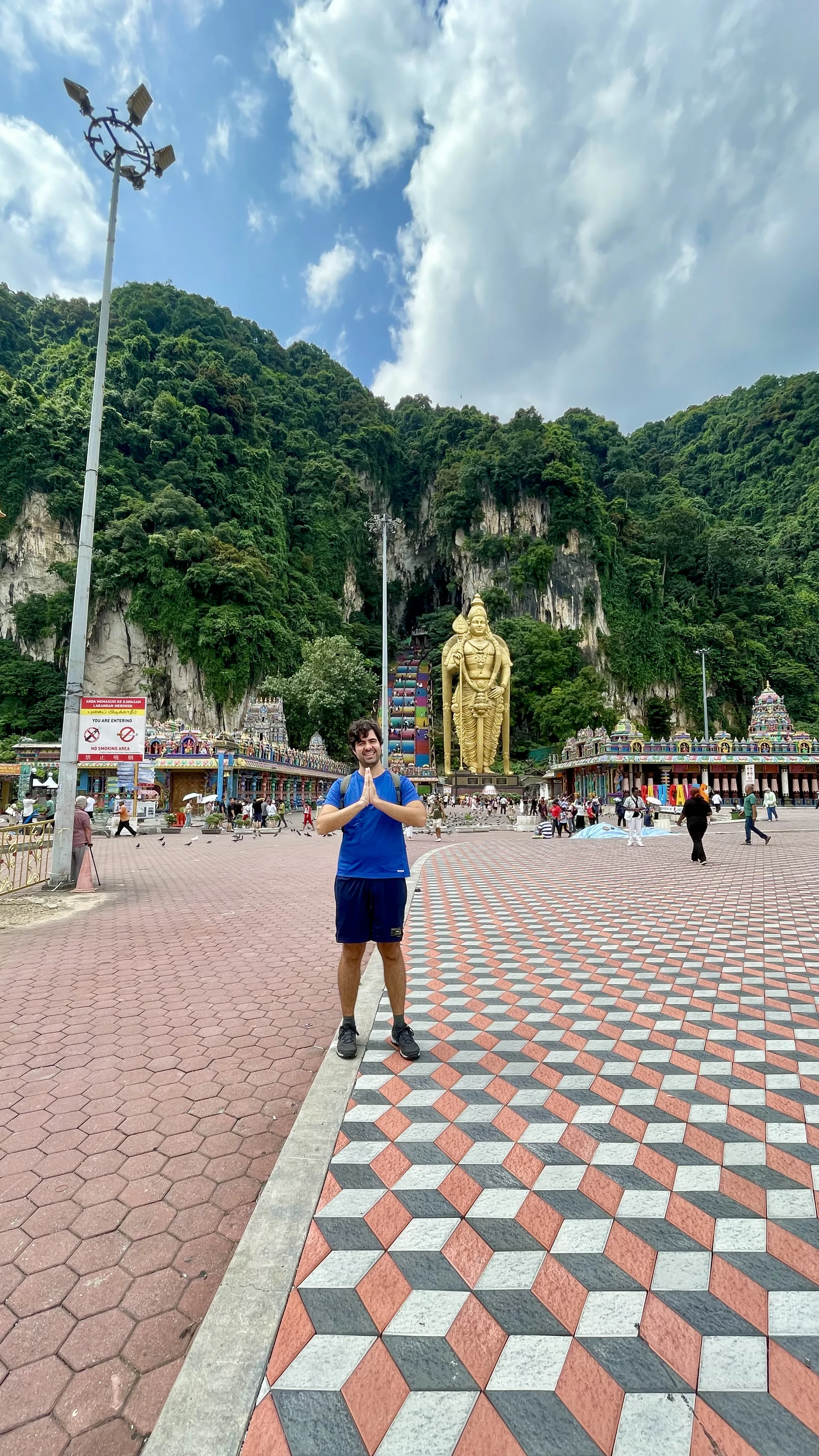 Um homem em pé com as mãos unidas em gesto de reverência diante da imensa estátua dourada de Murugan em Batu Caves, na Malásia.