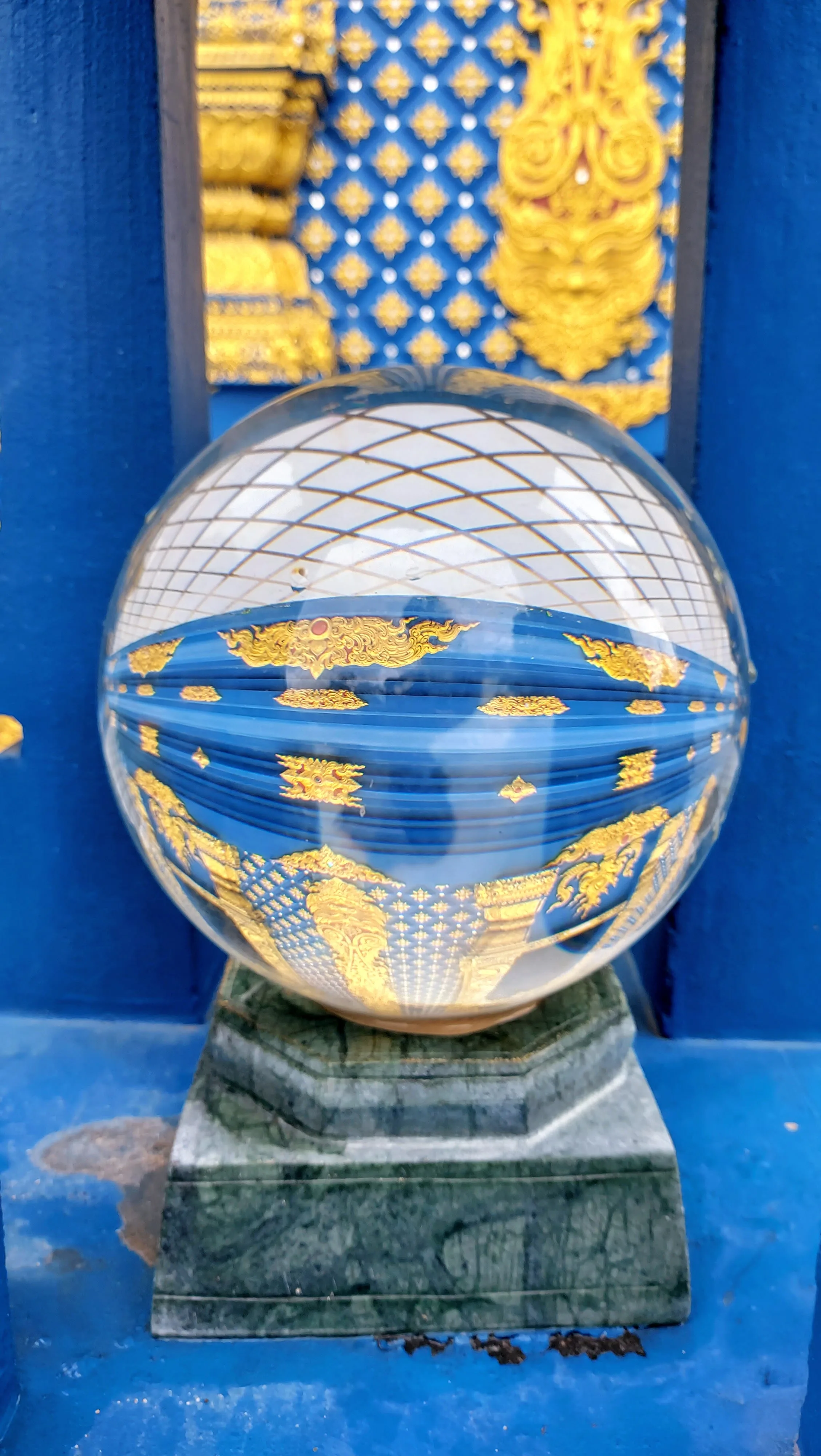 Esfera de vidro cristalina refletindo folhas verdes e o céu azul no Templo Azul em Chiang Rai, na Tailândia.