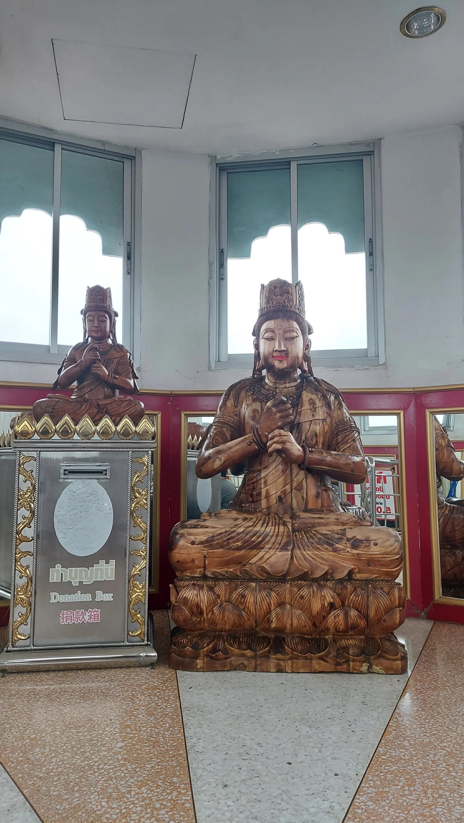 estátua de Buda esculpida em madeira em posição sentada ao lado de uma caixa de doações em um templo em Chiang Rai.