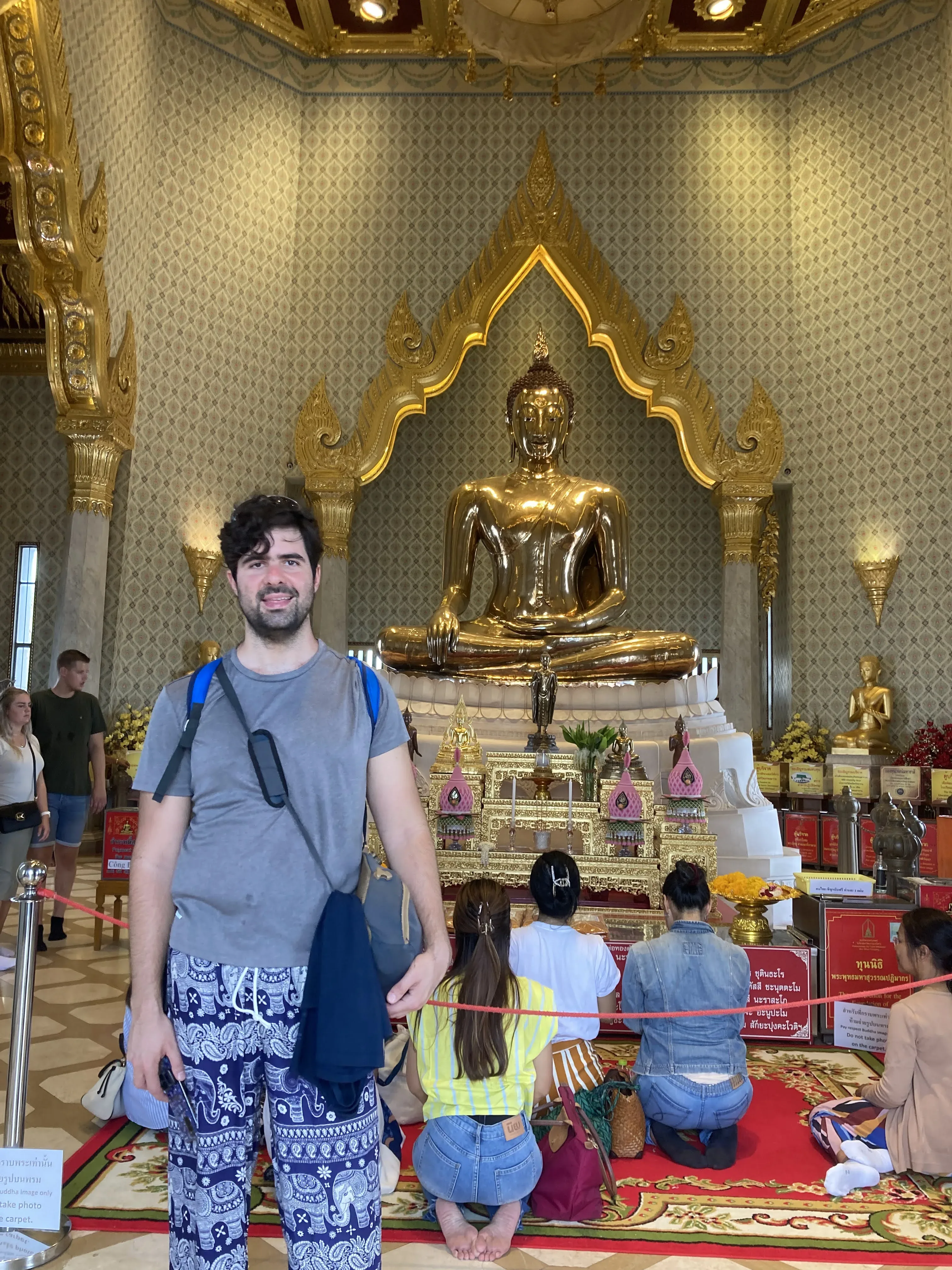 Um homem em pé em primeiro plano com estátua de Buda de ouro no altar do templo Wat Traimit em Banguecoque.