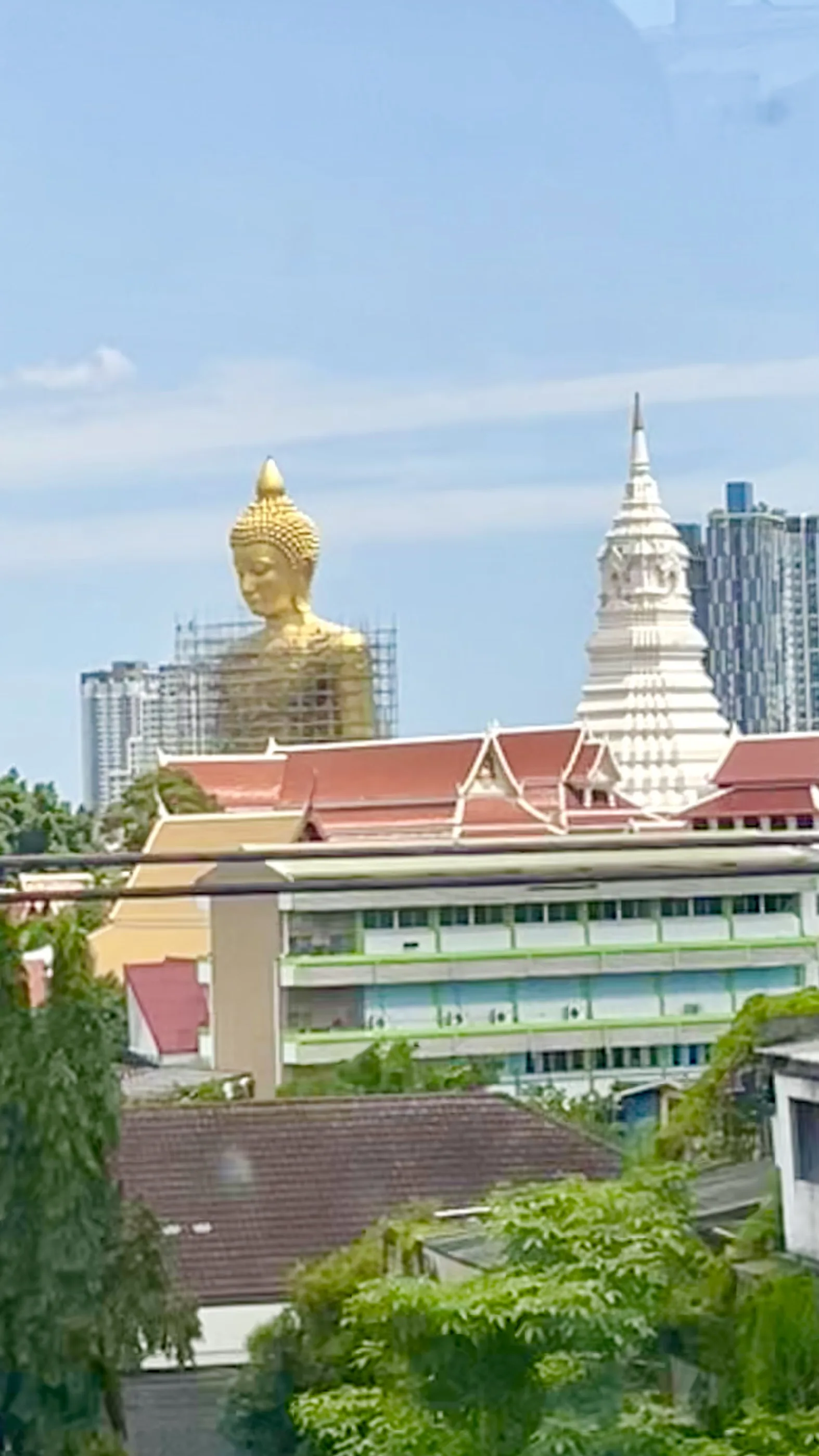 Vista distante da imponente estátua gigante de Buda em ouro e da torre branca no horizonte urbano de Banguecoque.