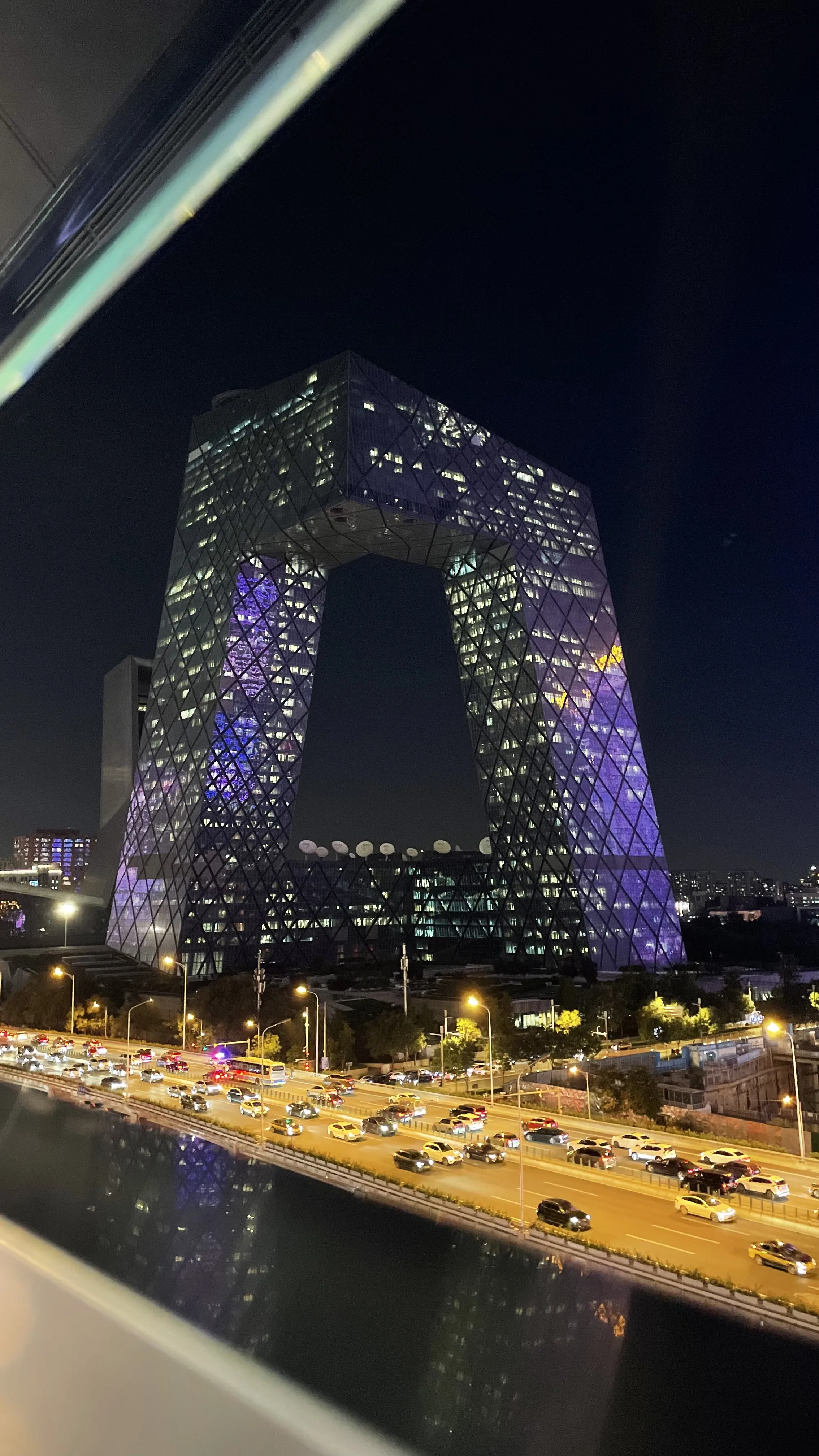 Sede da CCTV iluminada à noite com arquitetura em loop e tráfego intenso na avenida em Pequim.