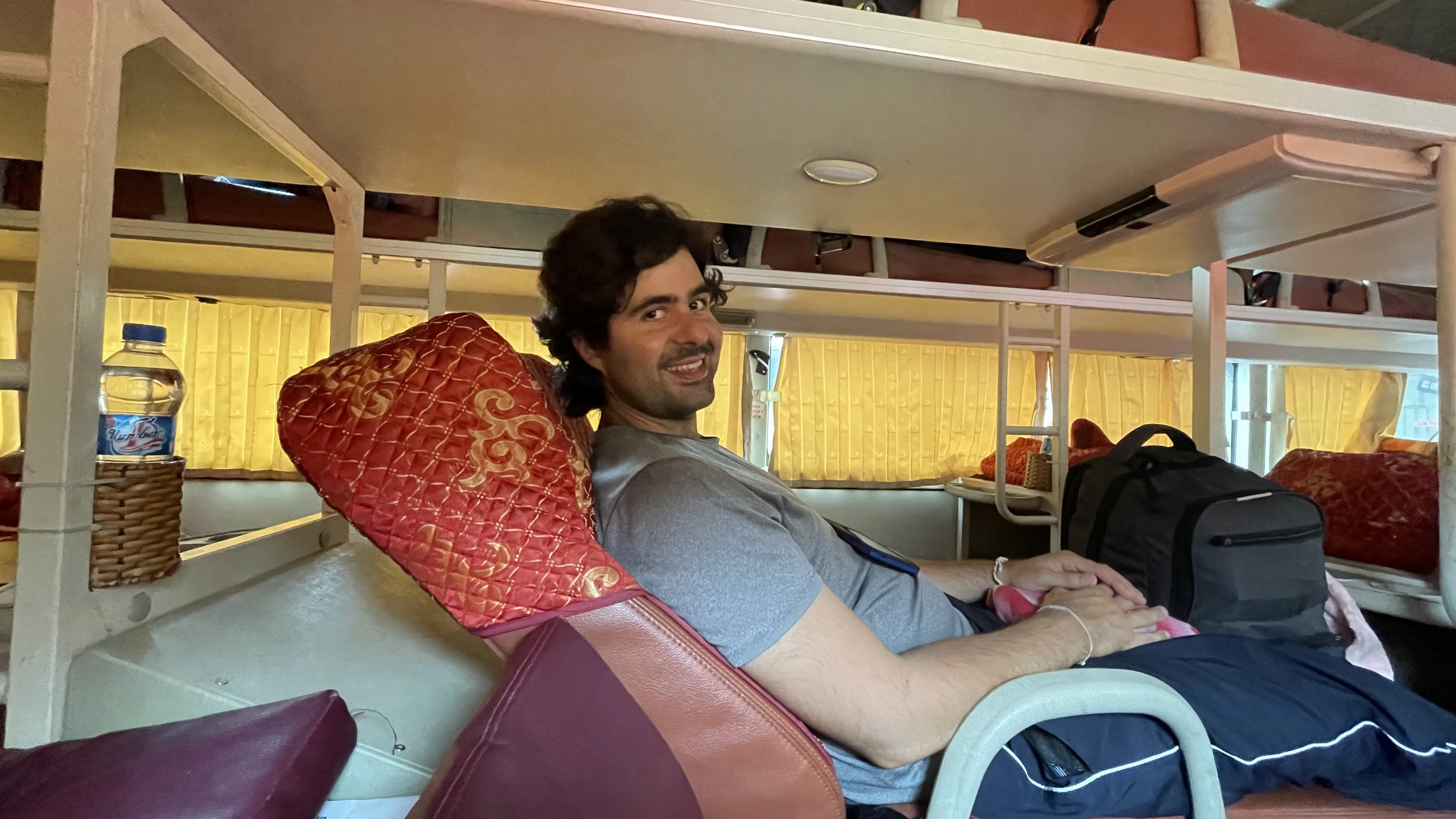 Homem sorridente sentado confortavelmente no beliche superior de um autocarro-cama de longa distância no Vietname.