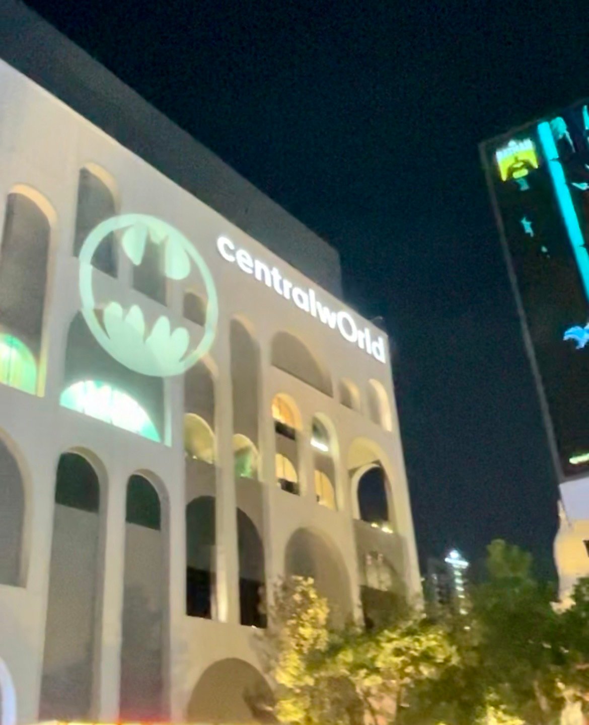 Fachada iluminada do shopping CentralwOrld à noite com projeção do símbolo do Batman em Banguecoque.