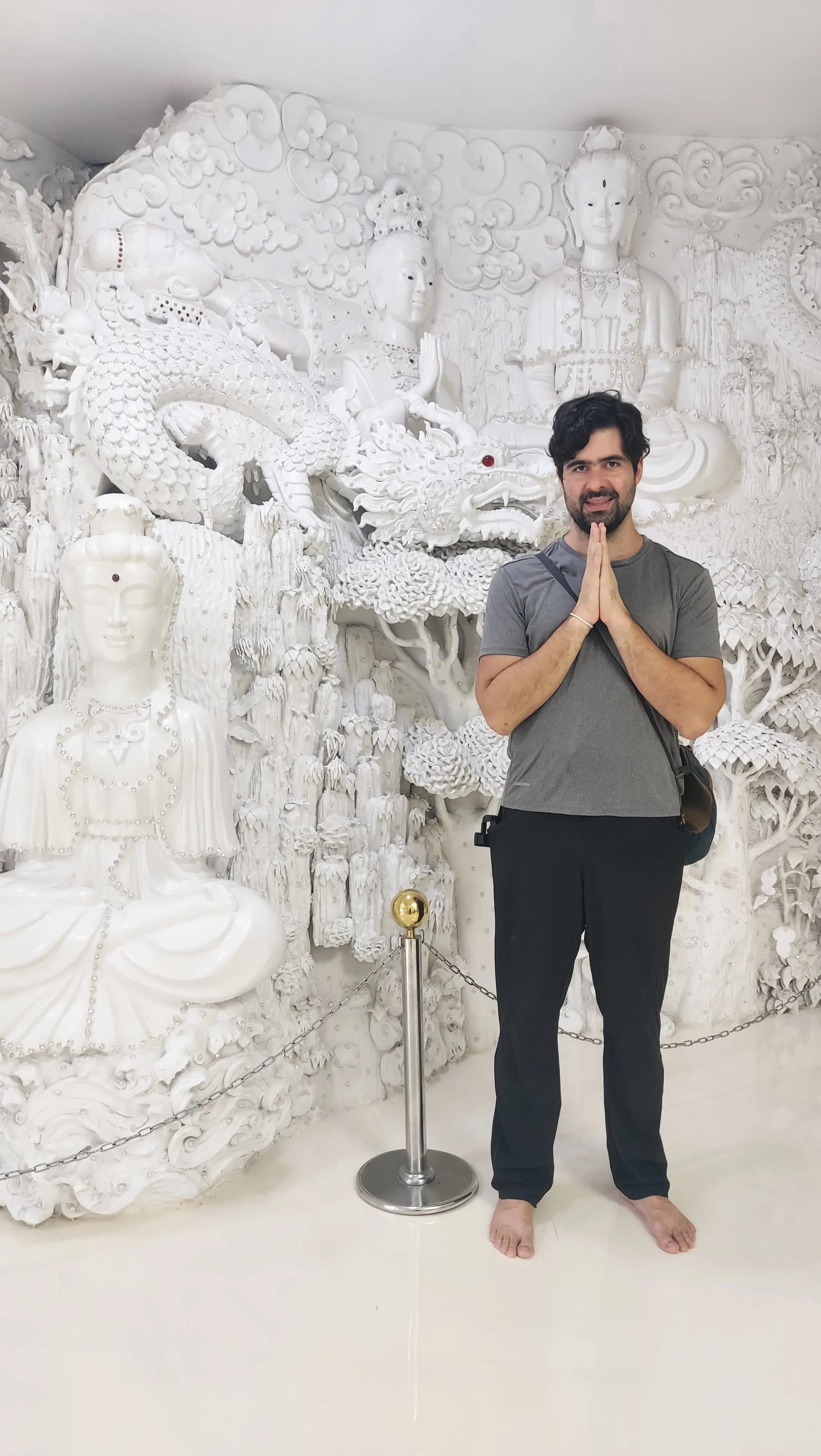 Um homem em pé com as mãos unidas em reverência no interior decorado em tons de branco do templo Wat Rong Suea Ten ou templo branco em Chiang Rai