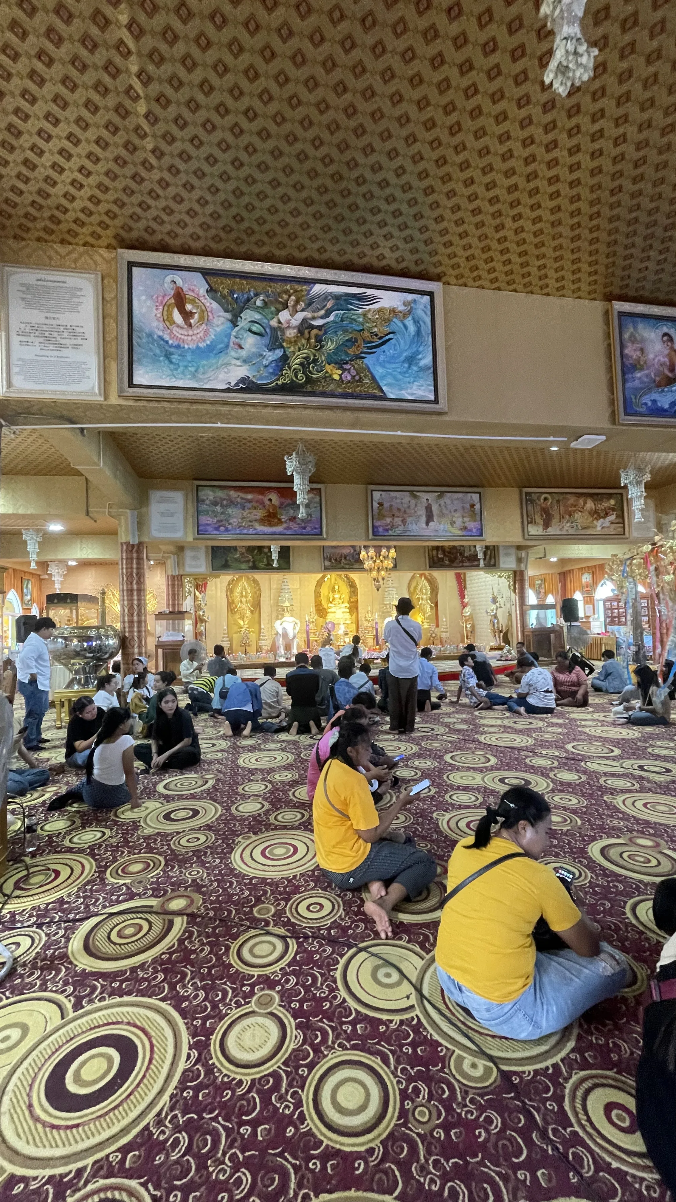 Visitantes e devotos sentados no piso do salão principal do templo Wat Phra That Pha Sorn Kaew aguardando a chuva passar