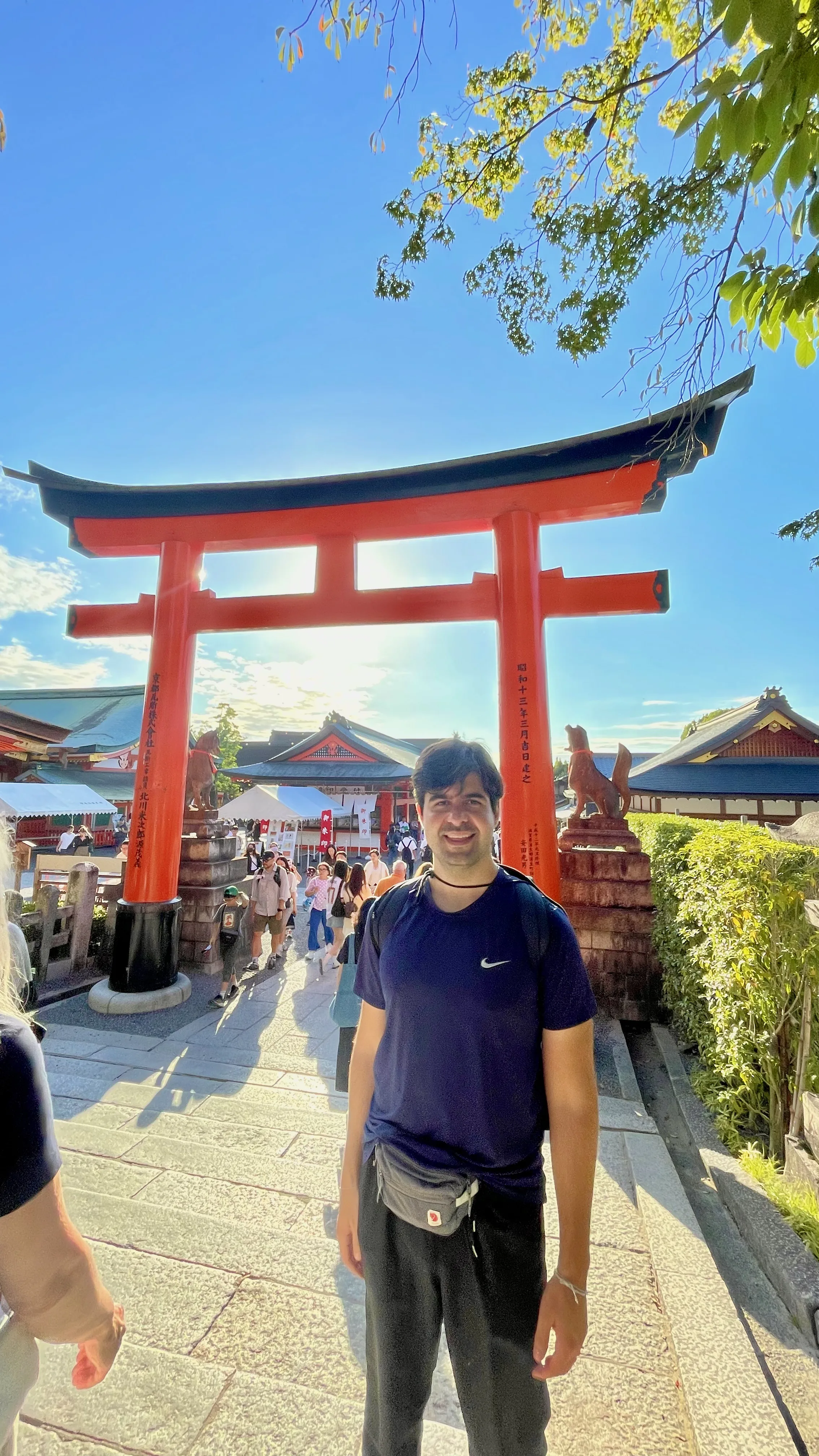 Visitante em pé diante do imponente portão torii vermelho na entrada do Santuário Fushimi Inari, em Kyoto.