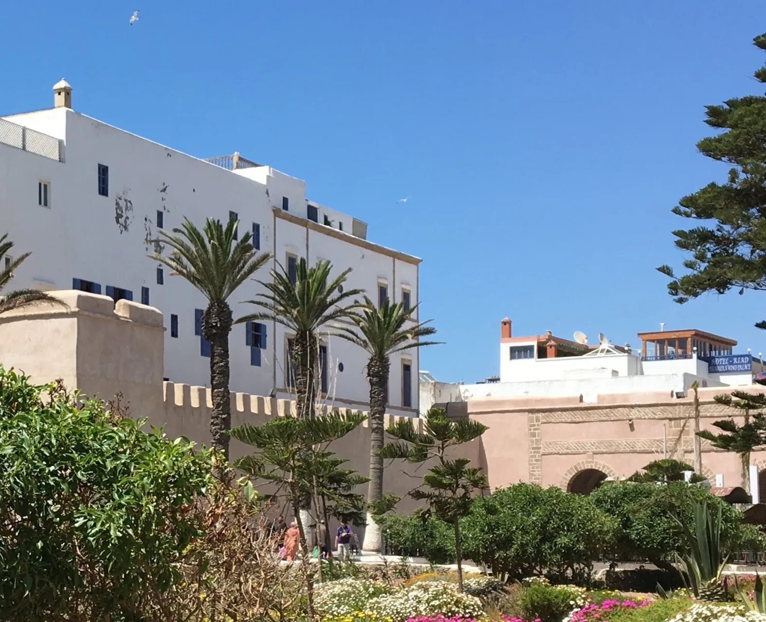 Praça com gramado verde e palmeiras em frente ao grande portão de pedra arqueado de Bab Marrakech e o bastião militar circular em Essaouira
