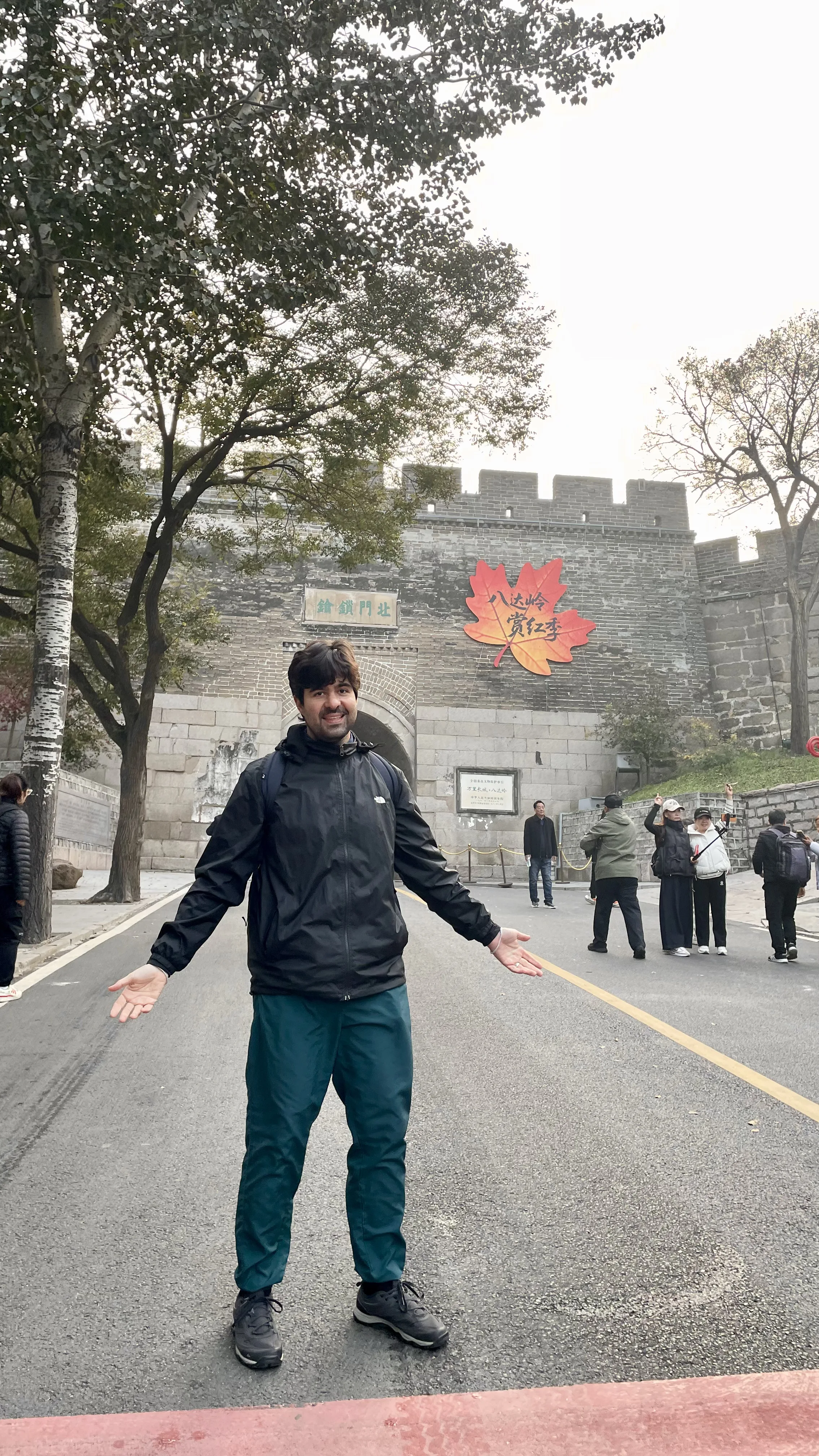 Turista sorrindo na entrada principal da Muralha da China em Badaling com portão histórico e folha de outono gigante