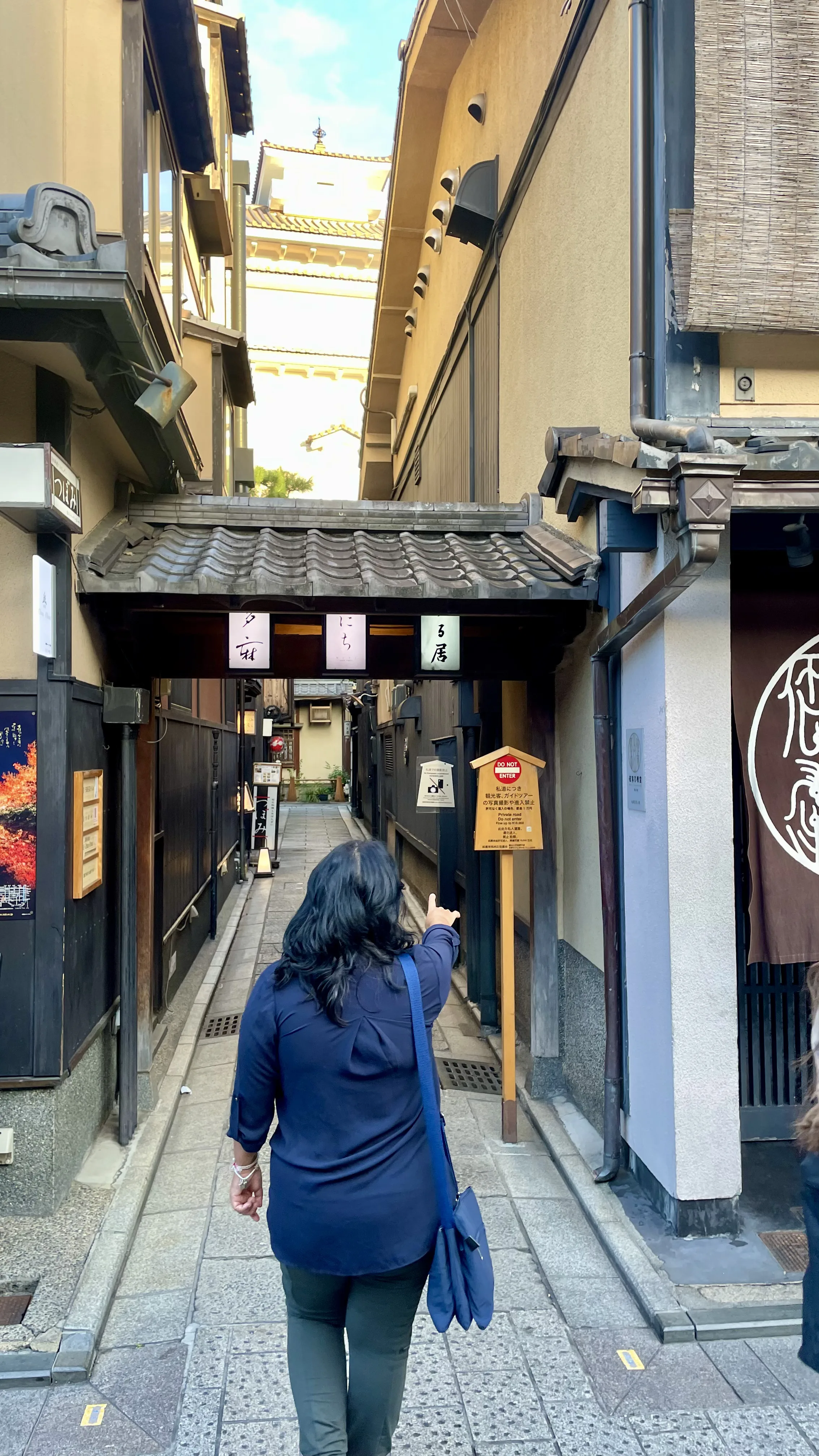 Mulher apontando para uma placa informativa na entrada de uma rua estreita e tradicional do bairro de Gion, em Kyoto.