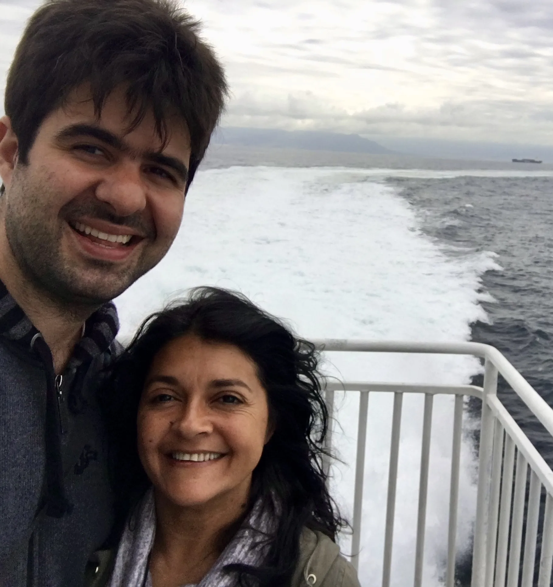 Um homem e uma mulher sorridentes em selfie a bordo de uma embarcação, com a esteira de espuma branca cortando as águas escuras do Estreito de Gibraltar ao fundo.