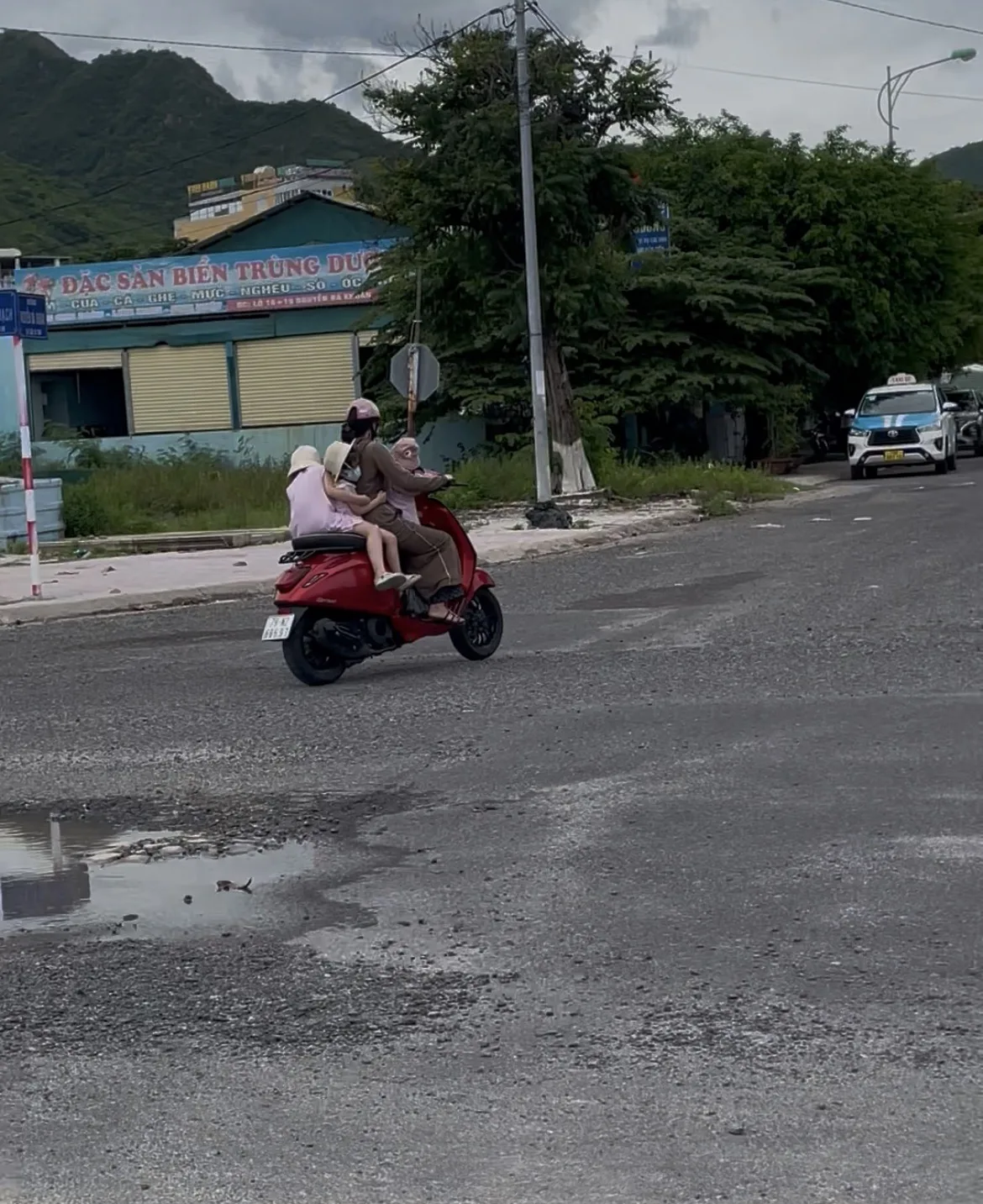 Família a circular de moto numa rua com edifícios e vegetação ao fundo no Vietname.