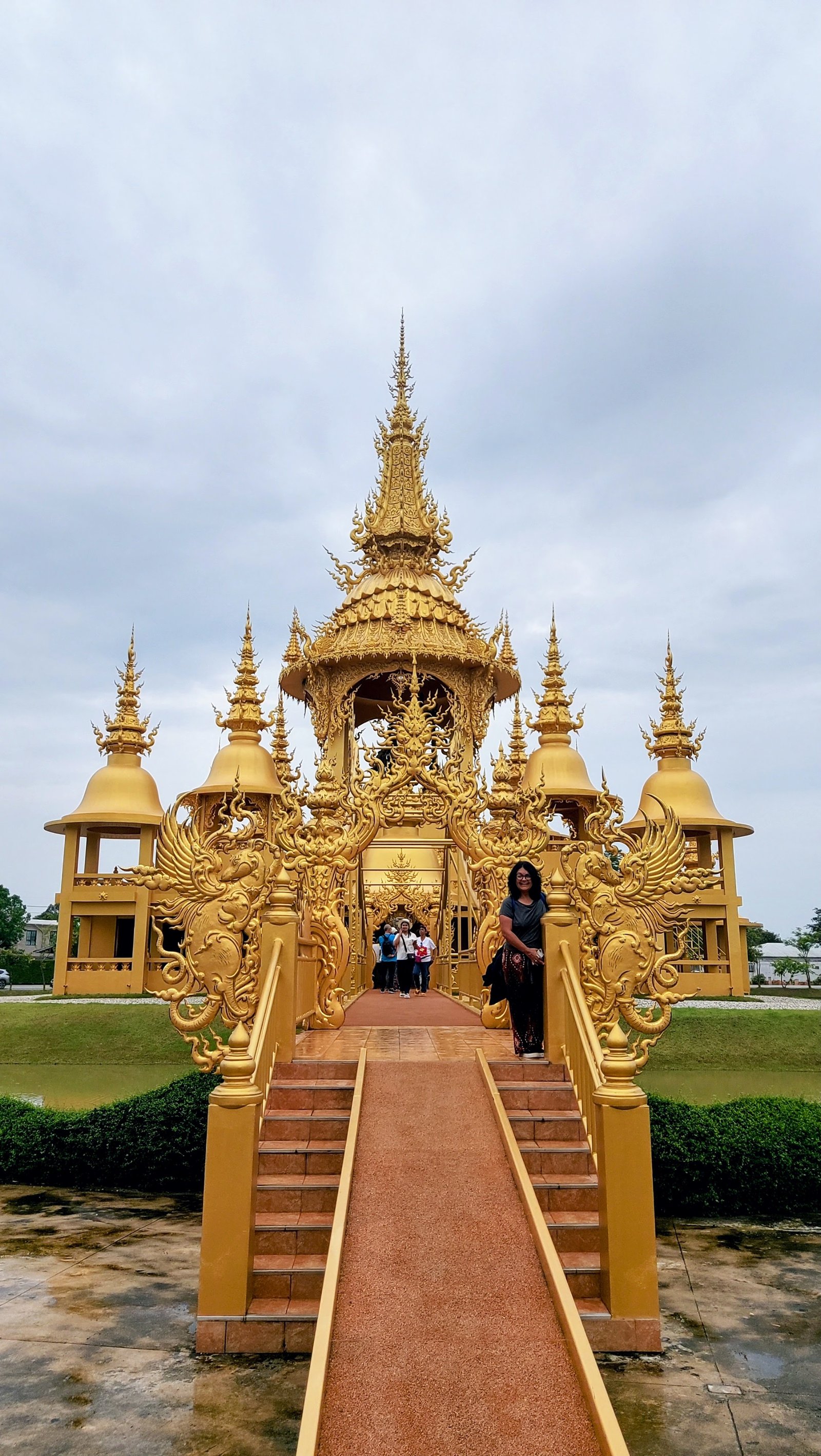 Uma mulher de pé na ponte de acesso ao pavilhão dourado dedicado a Ganesha no complexo do Templo Branco em Chiang Rai.