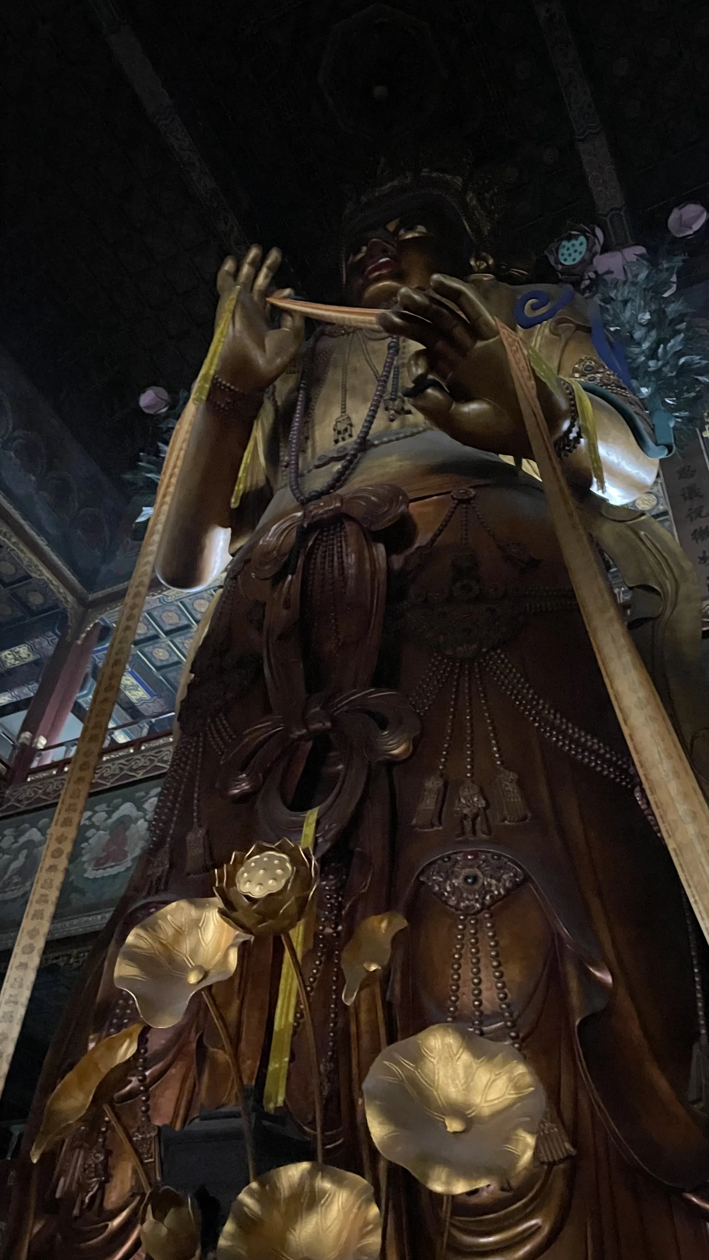 Estátua alta de Buda em madeira escura decorada com colares e fitas douradas no interior do Templo dos Lamas em Pequim.