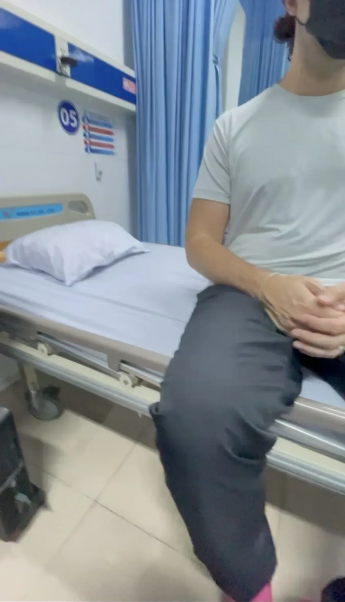 Paciente de máscara preta sentado na beira de uma maca com lençol branco em sala de emergência de hospital em Da Nang no Vietnã.