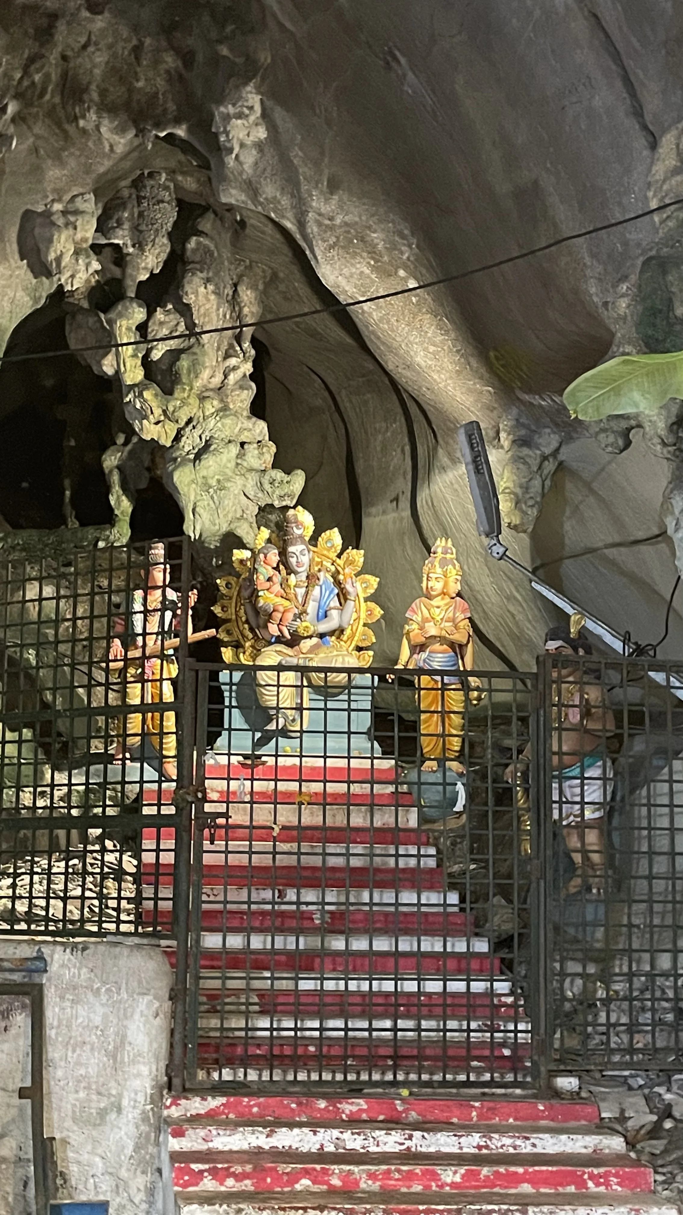 Estátuas de divindades hindus iluminadas e protegidas por grades vermelhas no interior das cavernas de Batu Caves.