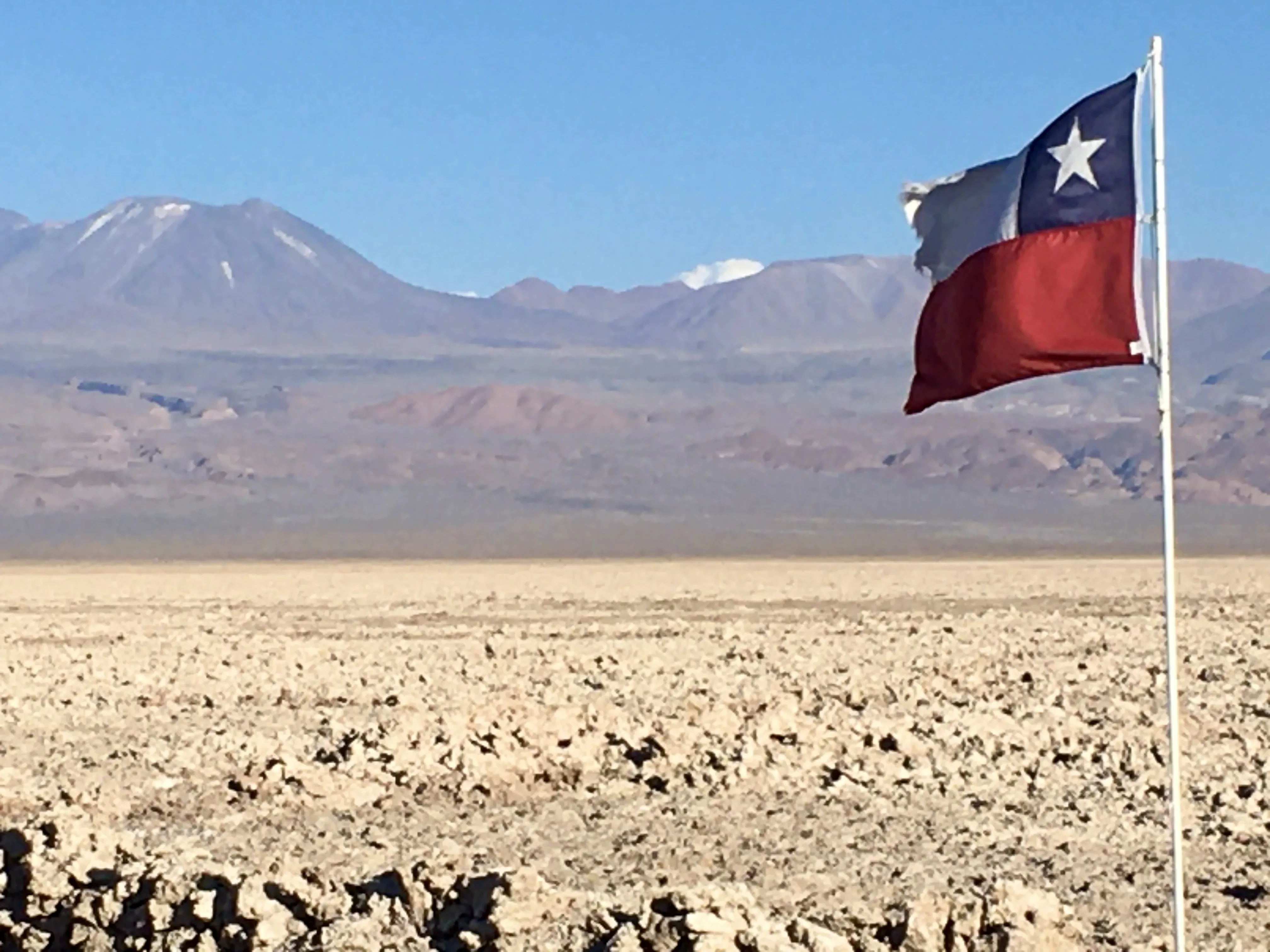 Bandeira do Chile balança ao vento diante do vasto e seco deserto de sal com montanhas ao fundo na Laguna Chaxa no Atacama.