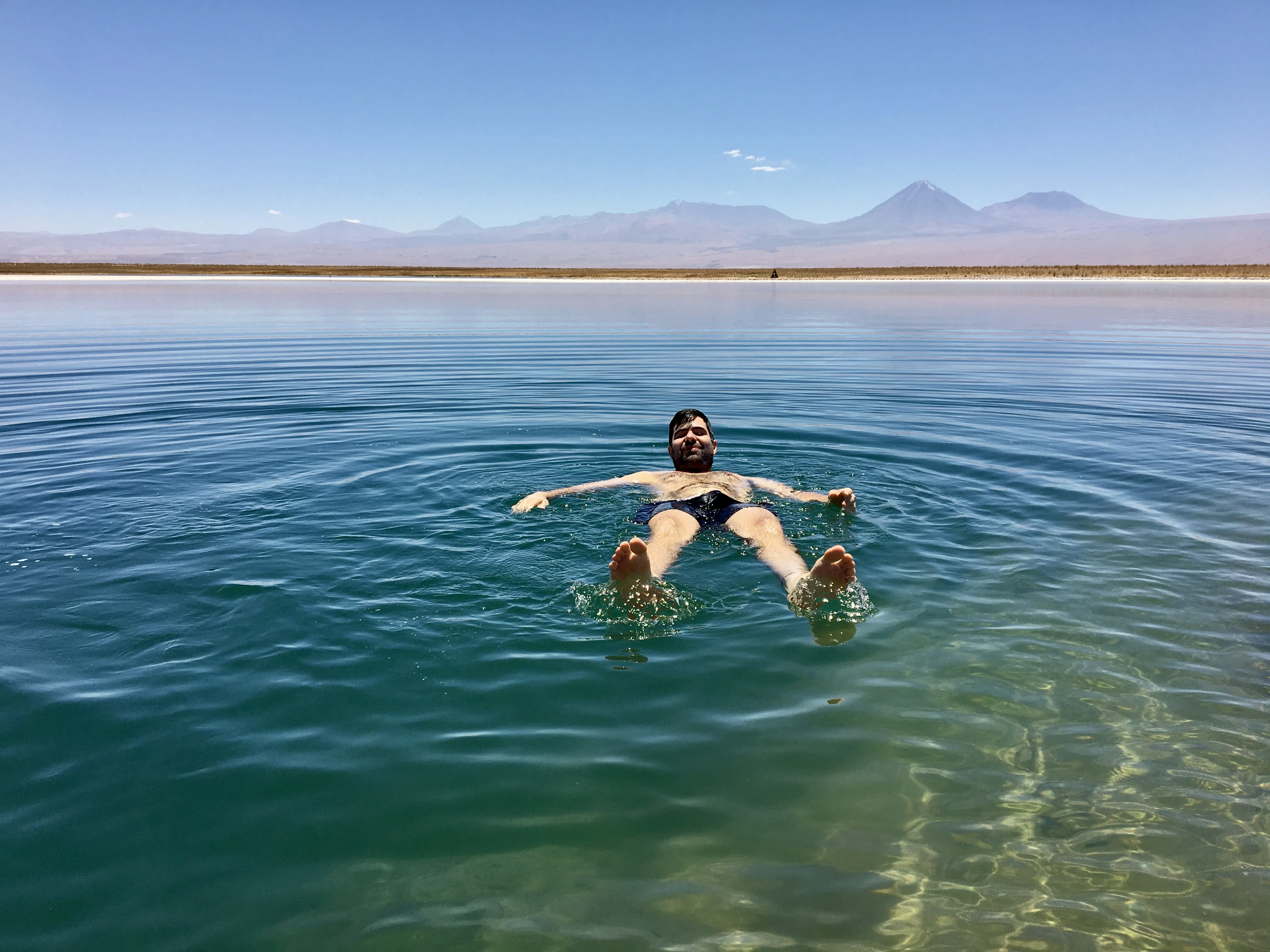 Homem flutua relaxado de barriga para cima nas águas cristalinas com montanhas ao fundo na bela Laguna Piedra no Chile.