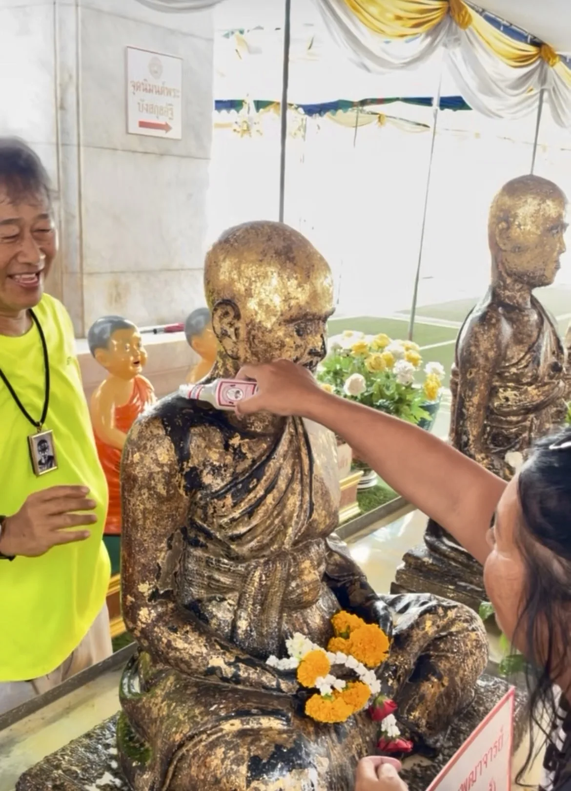 Pessoa limpando e despejando água sobre uma estátua dourada de Buda coberta com folhas de ouro em um templo tailandês.