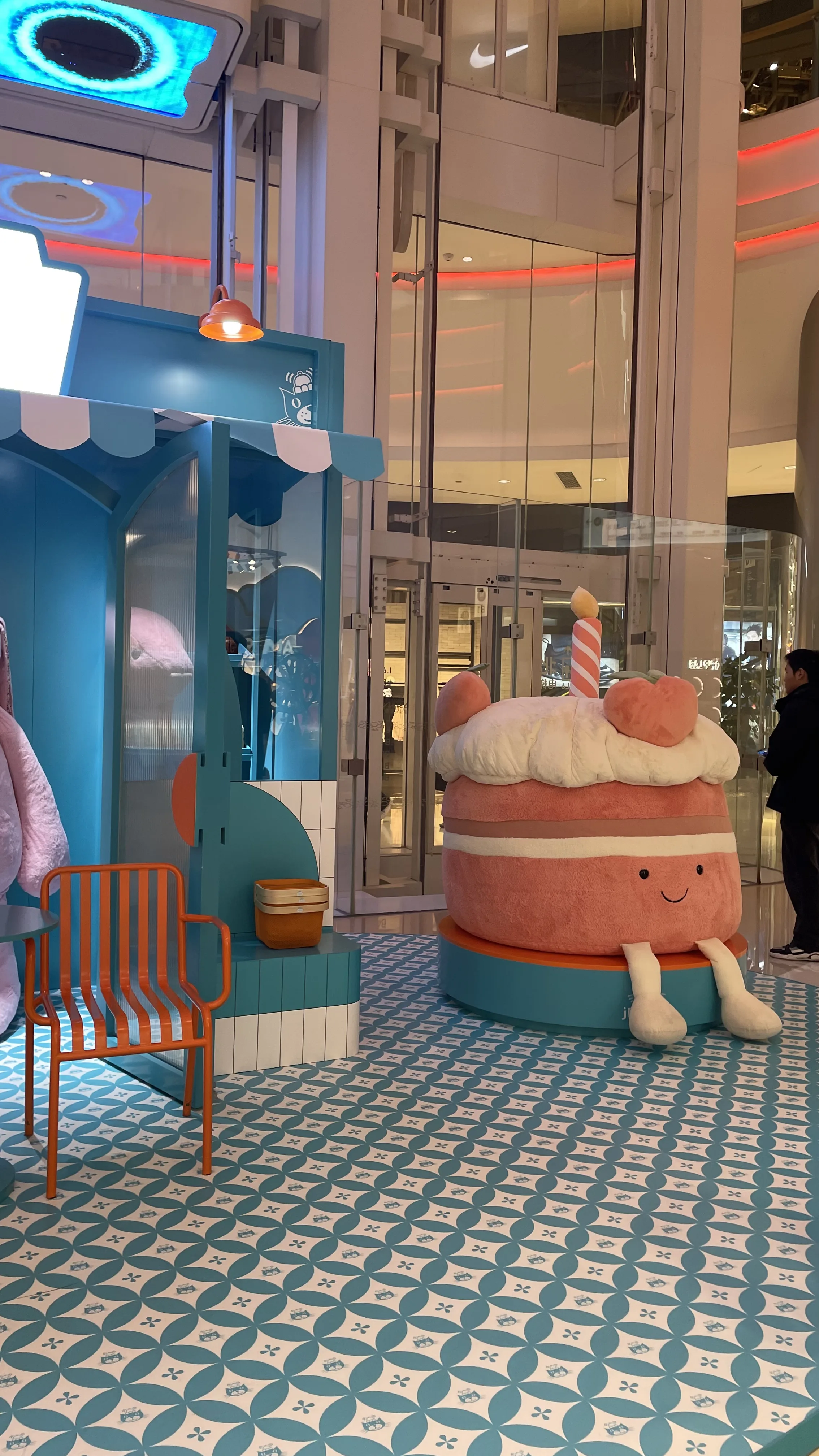 Decoração interna de shopping em Pequim com estrutura azul turquesa e boneco de pelúcia em formato de bolo de aniversário.