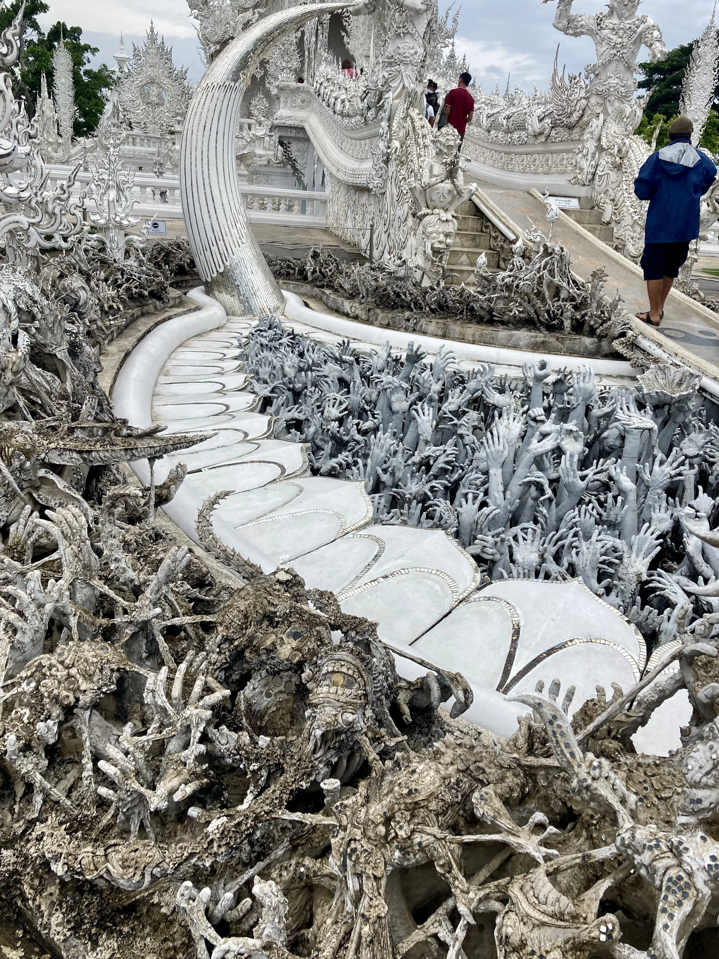 Detalhe das esculturas de mãos estendidas para o céu emergindo do solo ao longo da ponte de acesso no Templo Branco em Chiang Rai