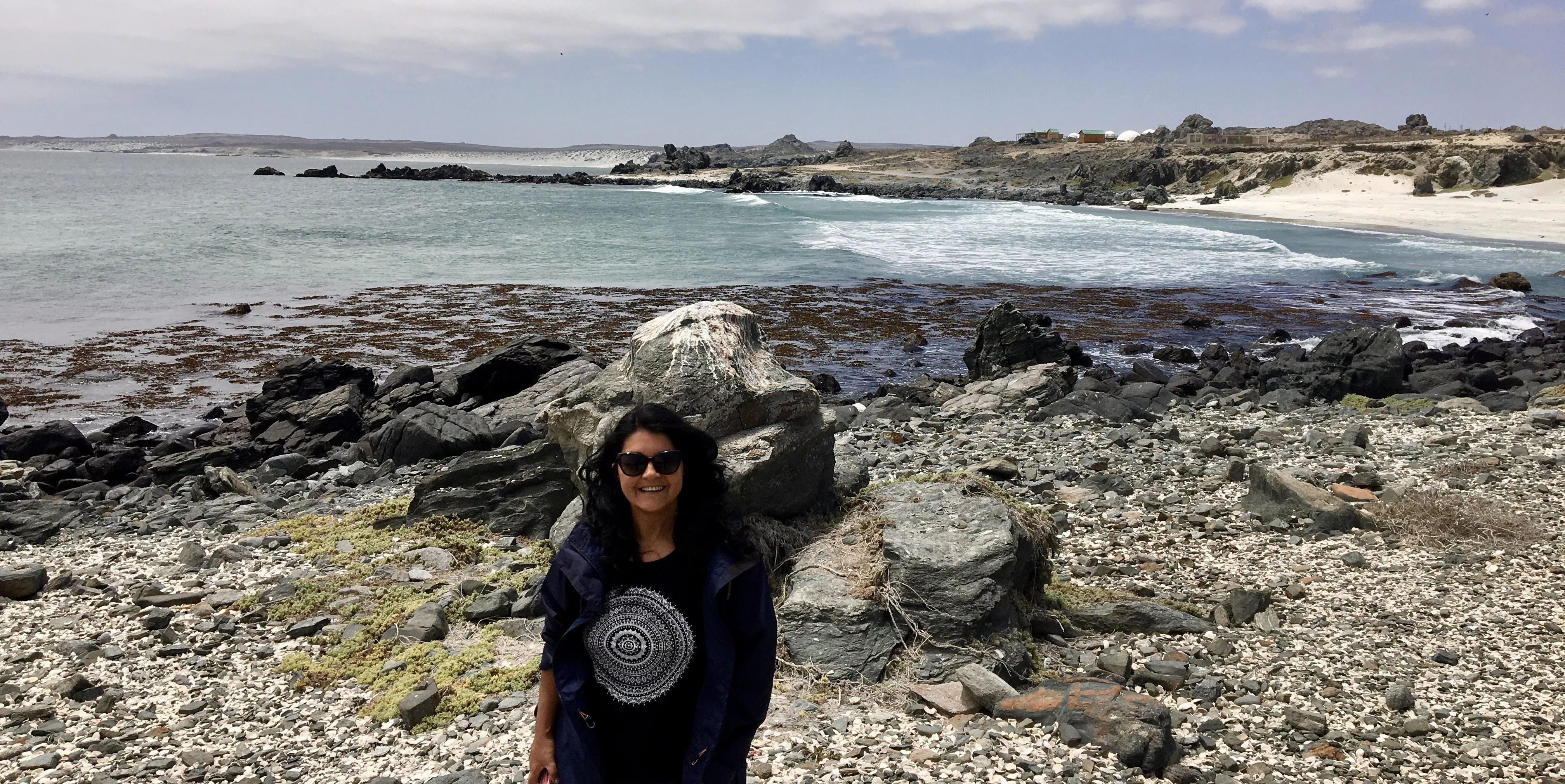 Mulher posando para foto na estrutura de madeira do Muelle de San Agustín, em Punta de Choros, com a imensidão azul do Oceano Pacífico ao fundo.