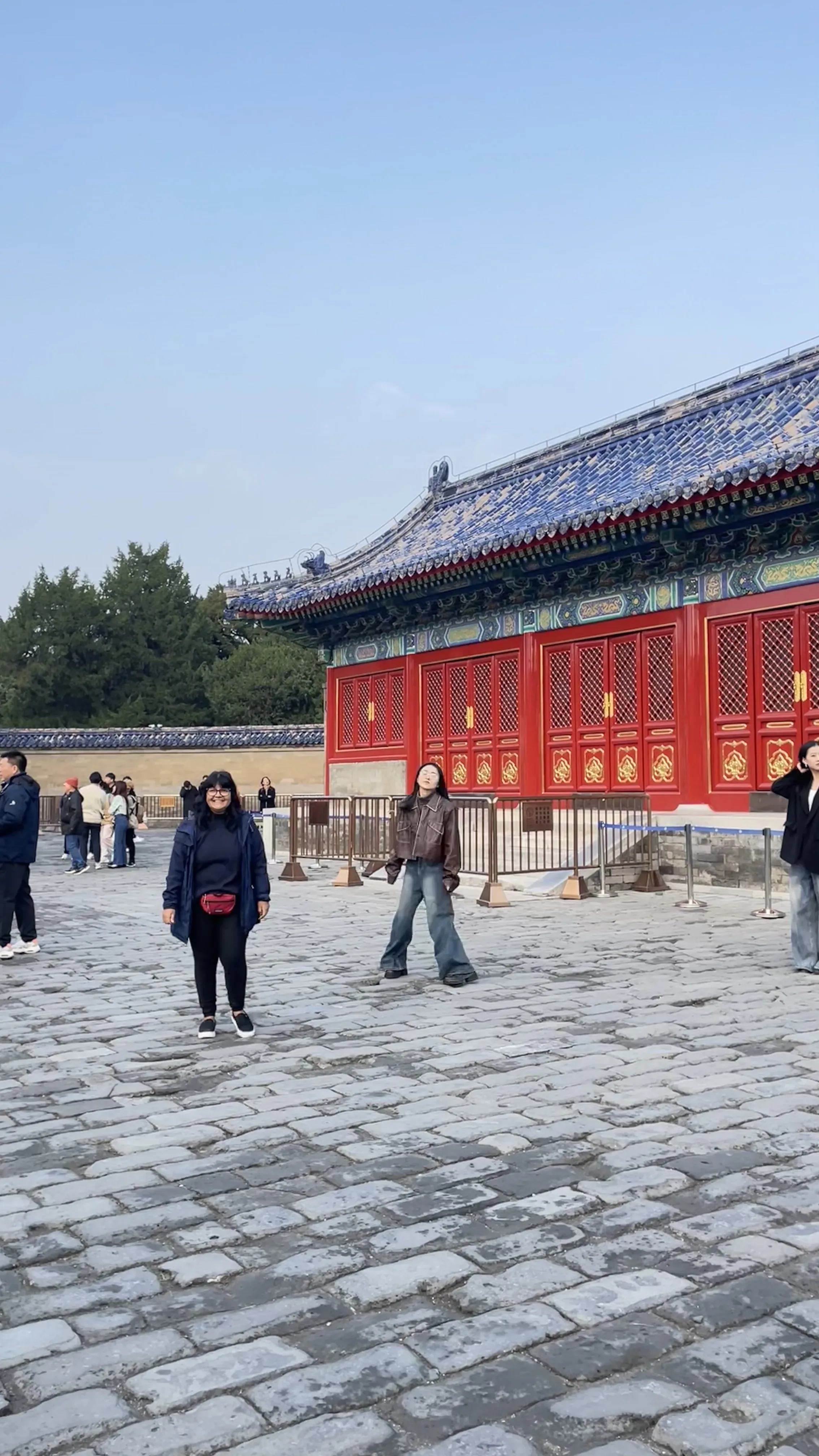 Mulher posa no pátio amplo com piso de pedra diante do portão monumental com detalhes em azul e vermelho no Templo do Céu em Pequim.