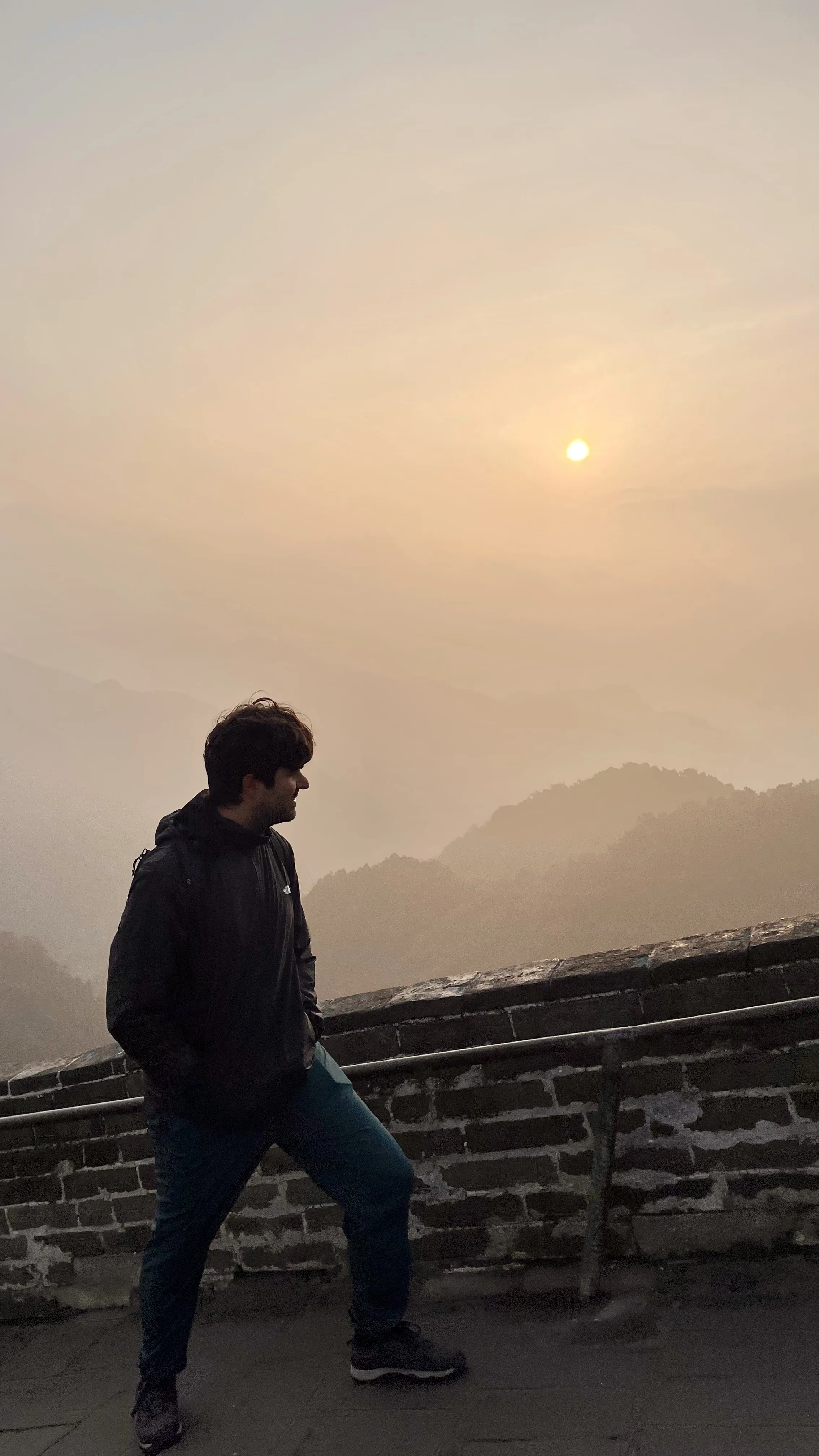 Homem contemplando o nascer do sol sobre as montanhas na Muralha da China durante expedição de viagem