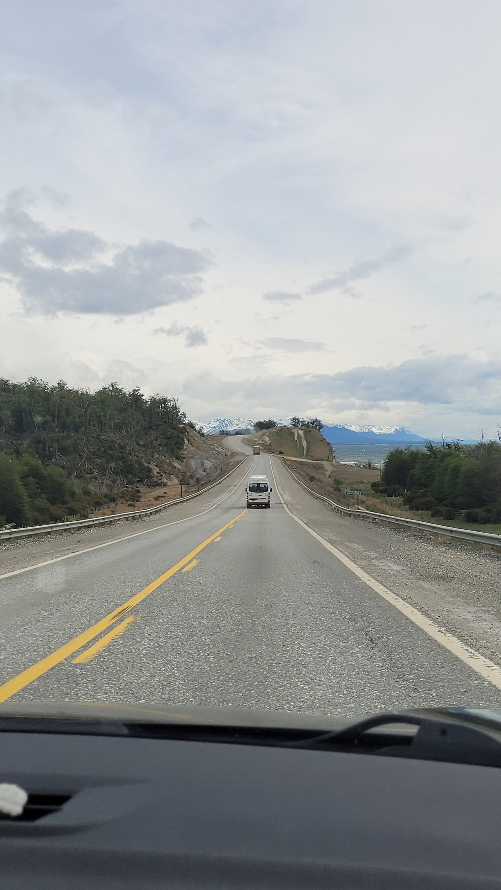 Vista da estrada asfaltada com linha amarela cortando a paisagem montanhosa e arborizada rumo a Ushuaia