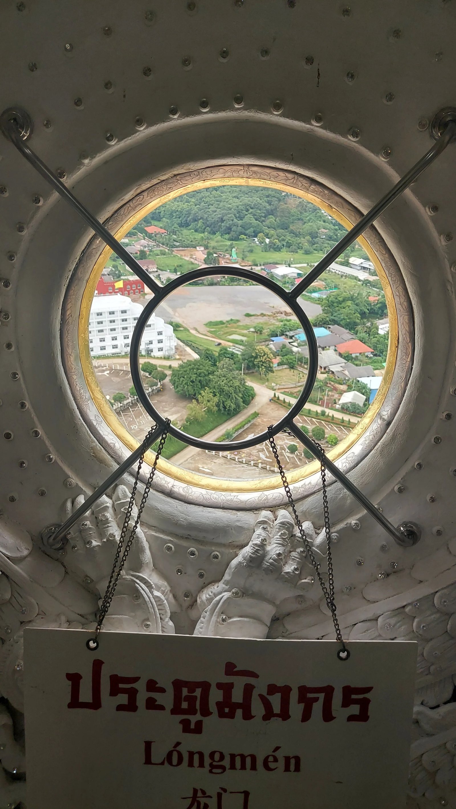 Vista aérea da paisagem urbana e verde através de uma abertura circular decorada com esculturas brancas e placa explicativa