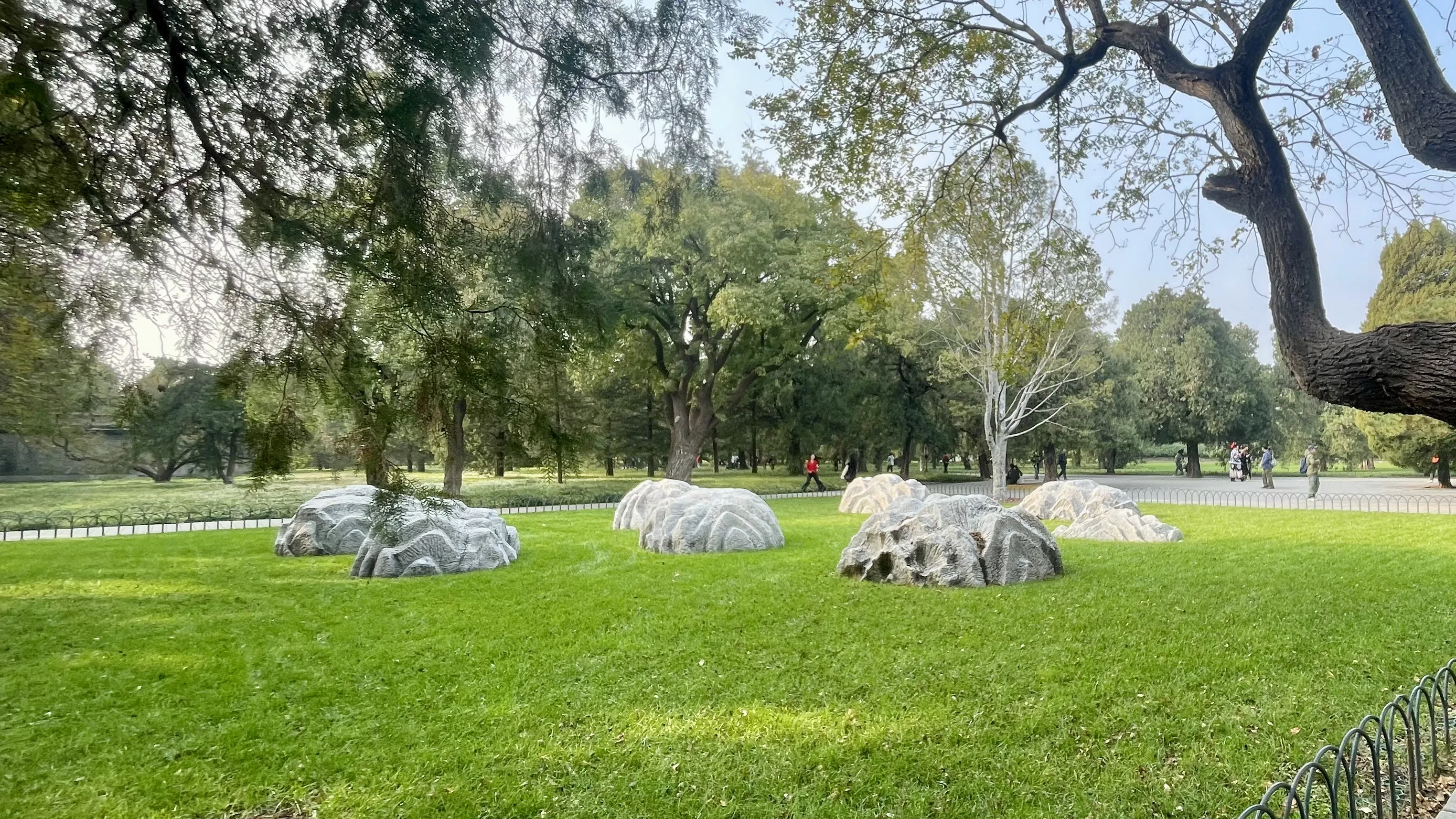 pedras antigas dispostas sobre a grama verde em área arborizada do Templo do Céu em Pequim.