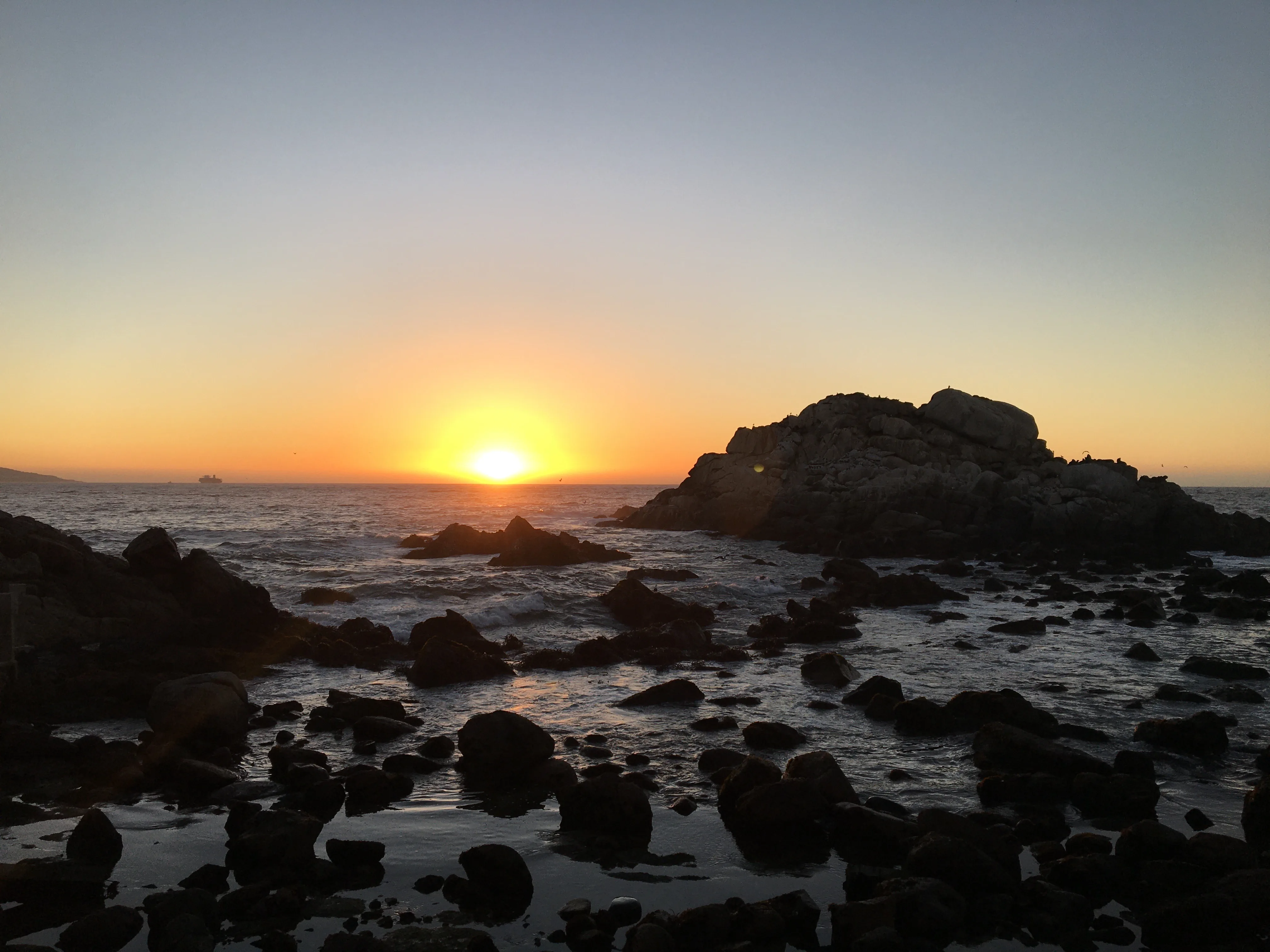 Pôr do sol na orla marítima de Viña del Mar com as ondas do Oceano Pacífico quebrando nas pedras ao fundo.