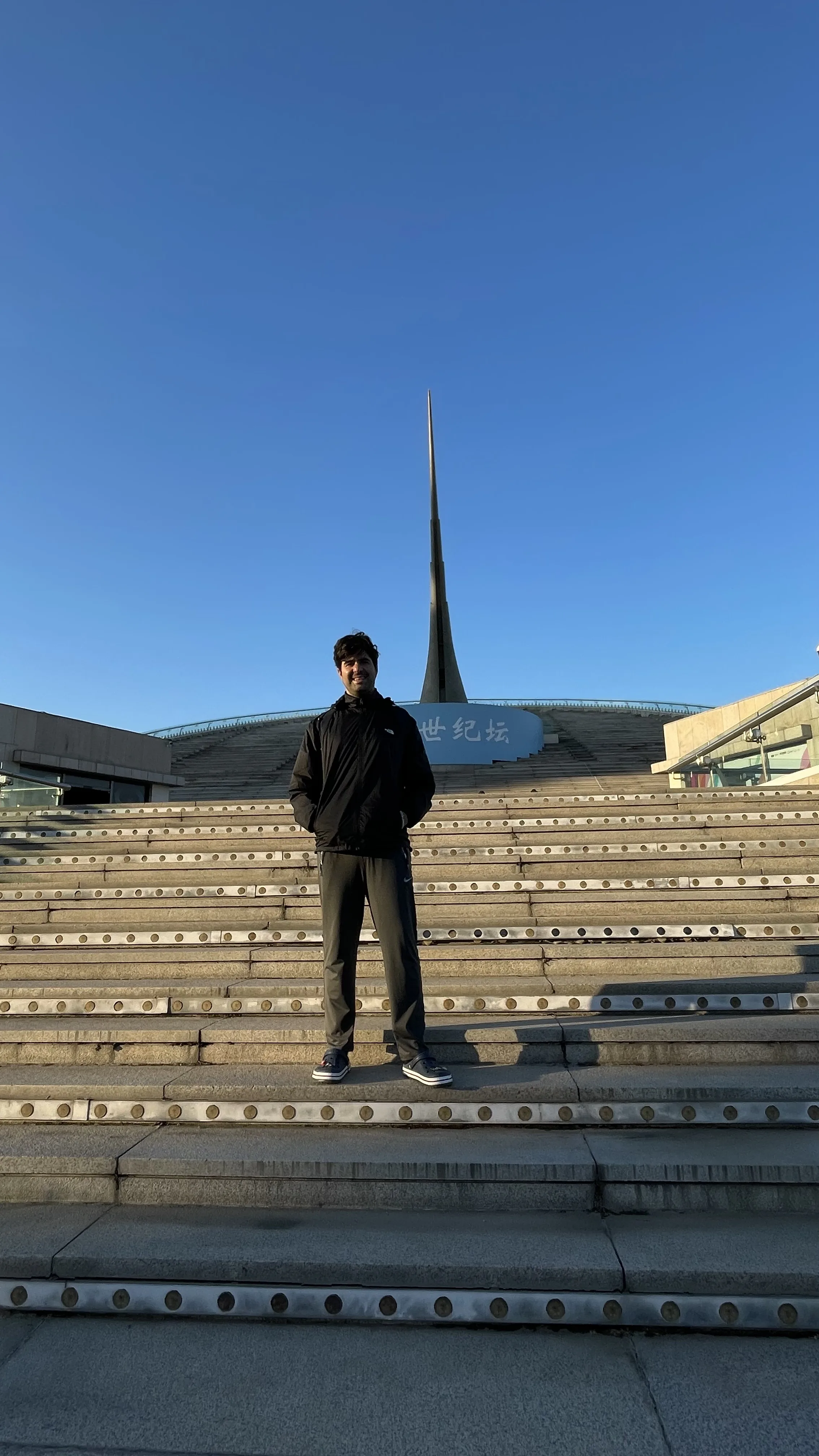 Homem de pé em ampla escadaria de pedra em frente à torre monumental do relógio de sol em Pequim.