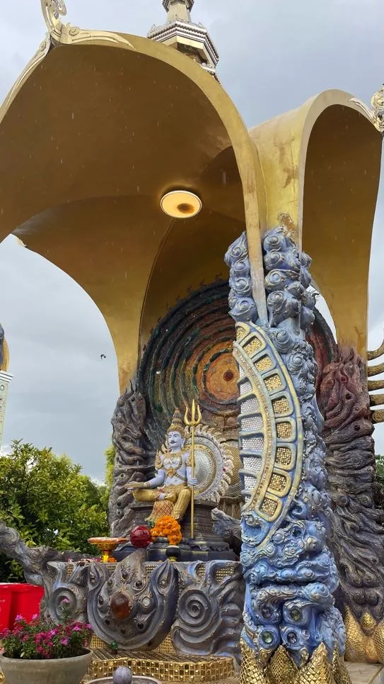 Estátua detalhada de divindade sob um dossel dourado ornamentado com colunas azuis texturizadas e decoração intrincada.