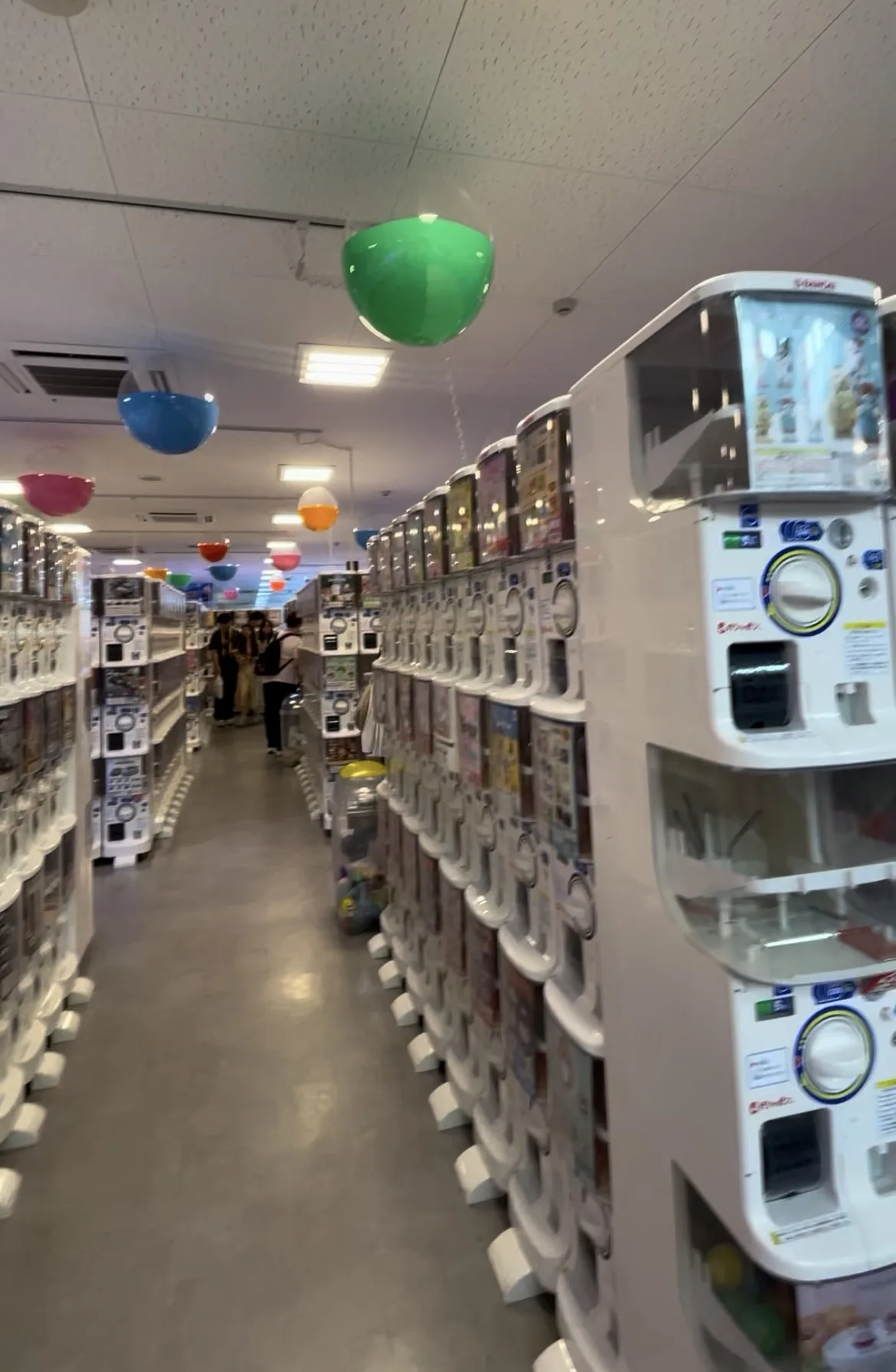 Corredor repleto de máquinas de brinquedos gachapon brancas com bolas coloridas penduradas no teto em Nara.