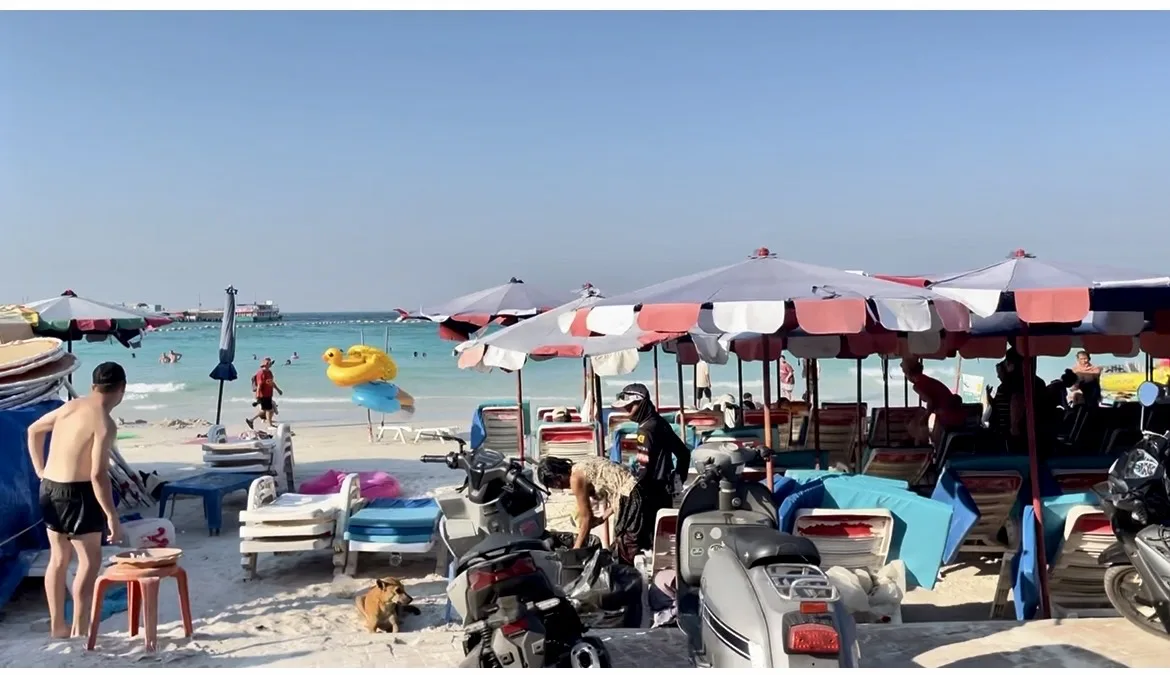 Movimento de turistas e barracas de praia com guarda-sóis coloridos na areia de Ko Lan
