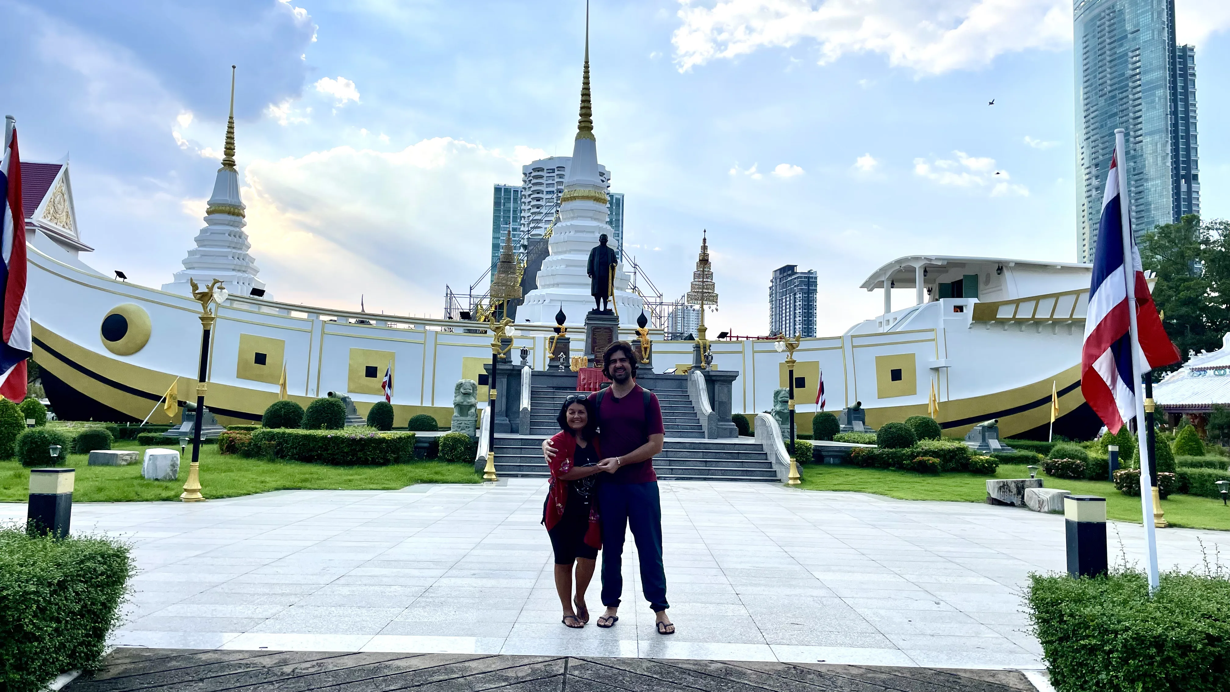 Casal em pé abraçado diante do formato de barco do Yan Nawa Temple à beira de um canal em Banguecoque.