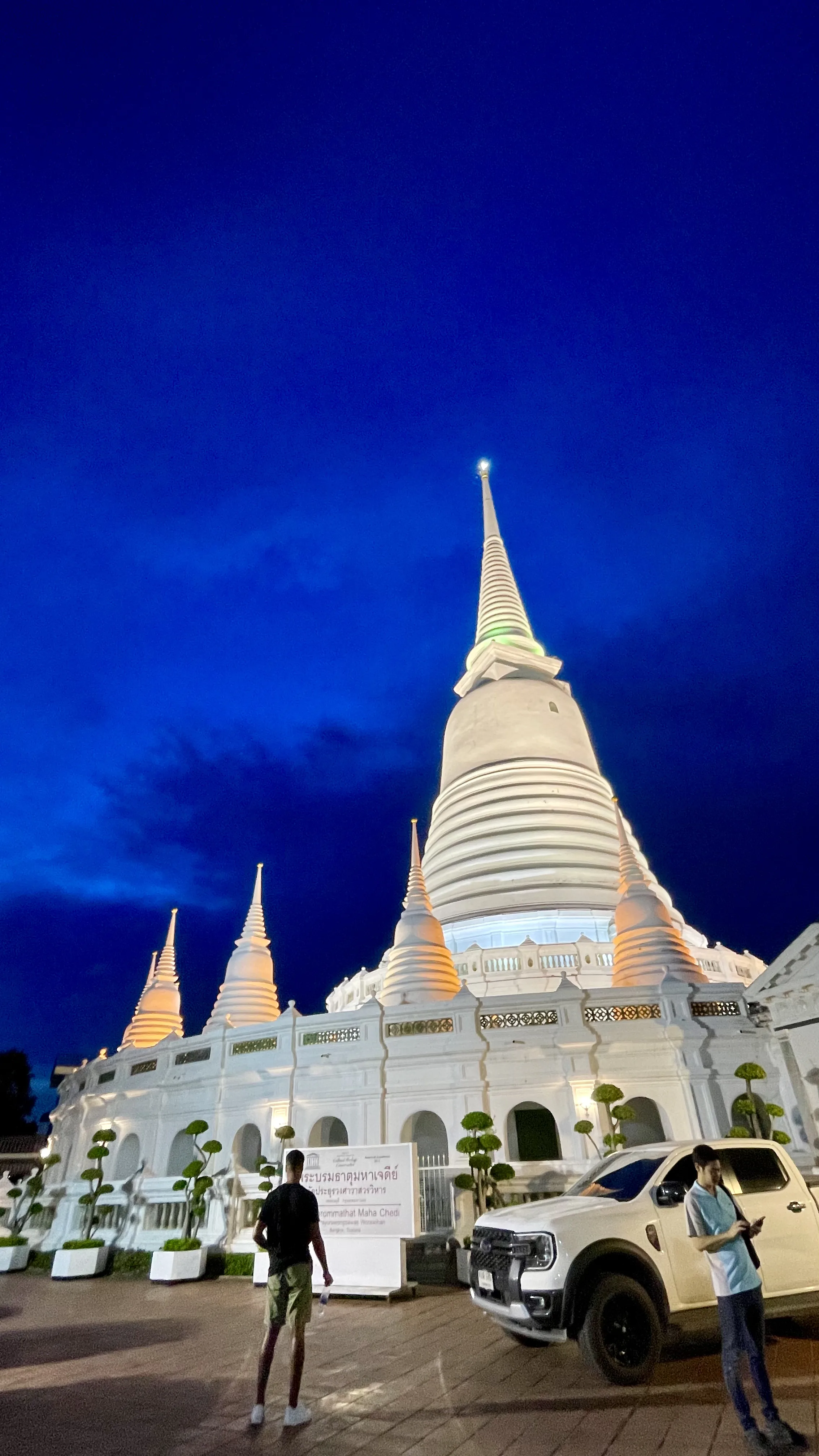 Grandes stupas brancas iluminadas do Wat Prayoon sob o céu azul profundo ao anoitecer em Banguecoque.