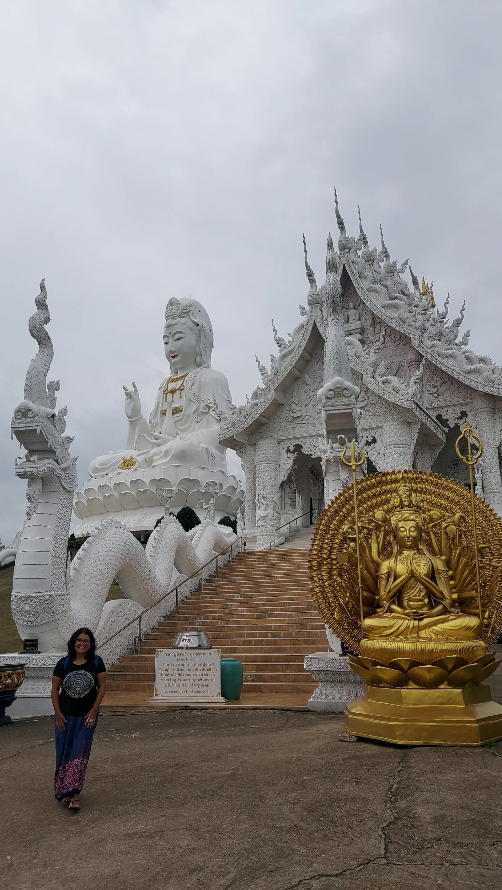 Uma mulher em pé ao lado da imponente estátua branca e da estátua dourada de Guanyin no complexo do templo em Chiang Rai