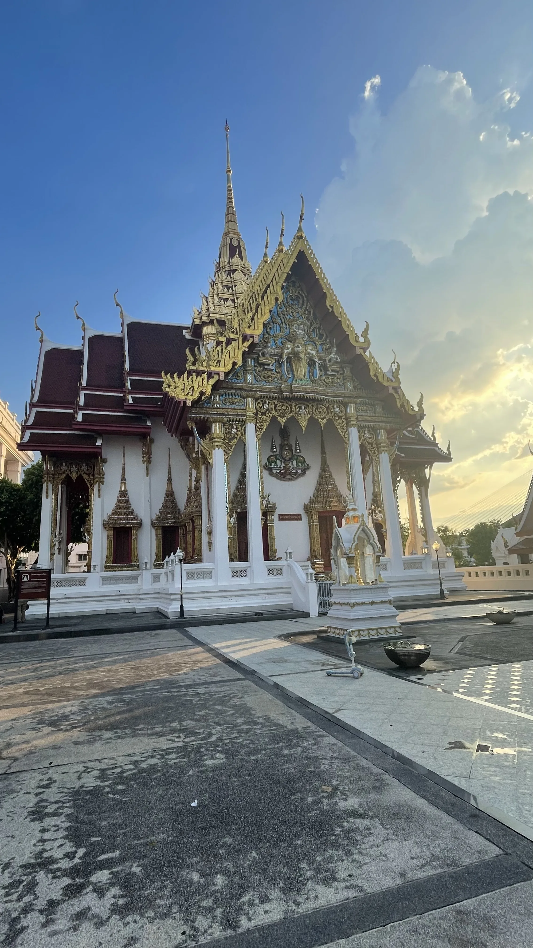 Fachada principal e arquitetura ornamentada em branco e dourado do Wat Devaraj Kunchorn, em Banguecoque, sob céu azul ao entardecer.