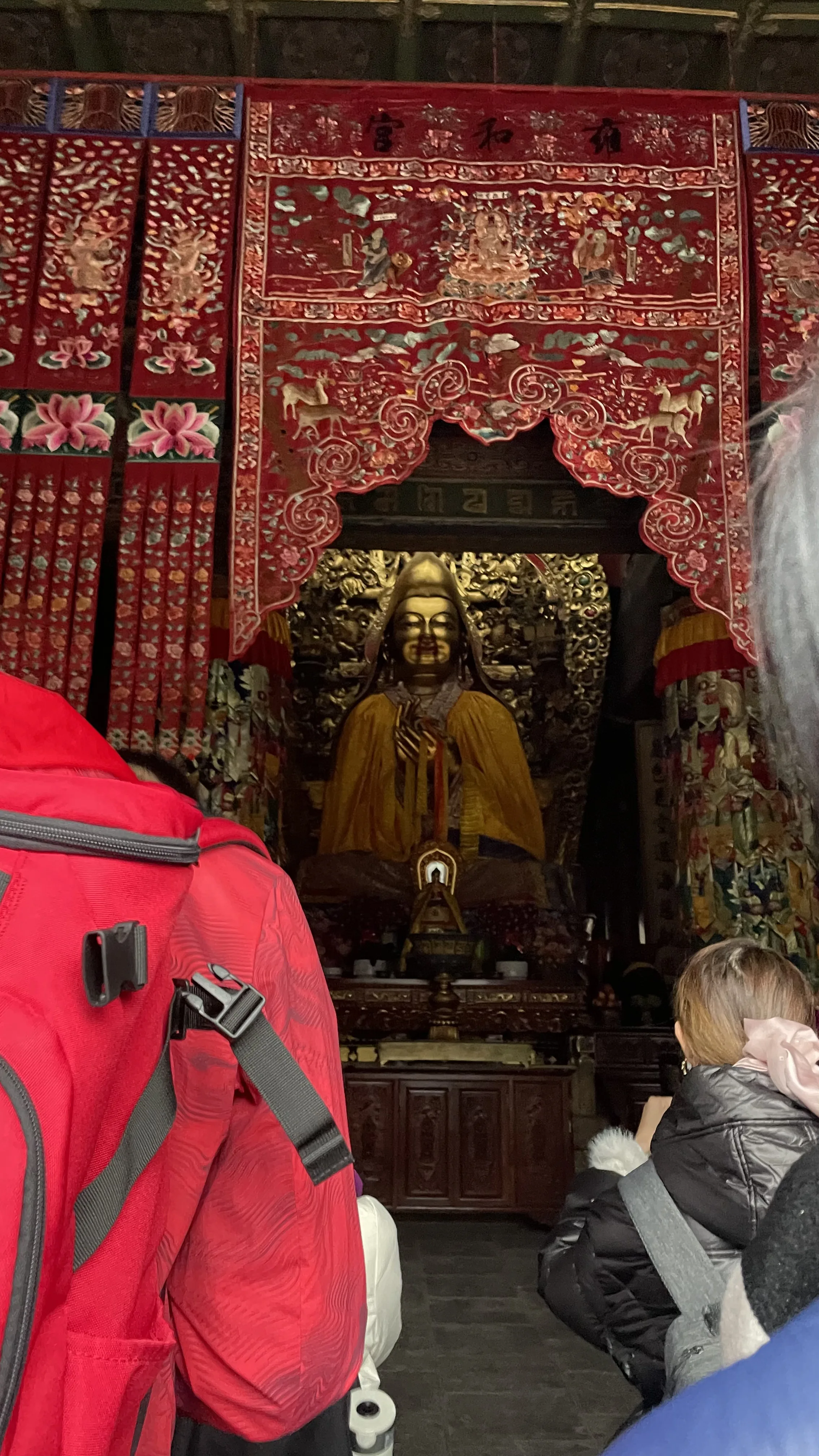 Estátua de Buda em destaque sob dossel de tecido vermelho decorado com bordados em santuário budista em Pequim.