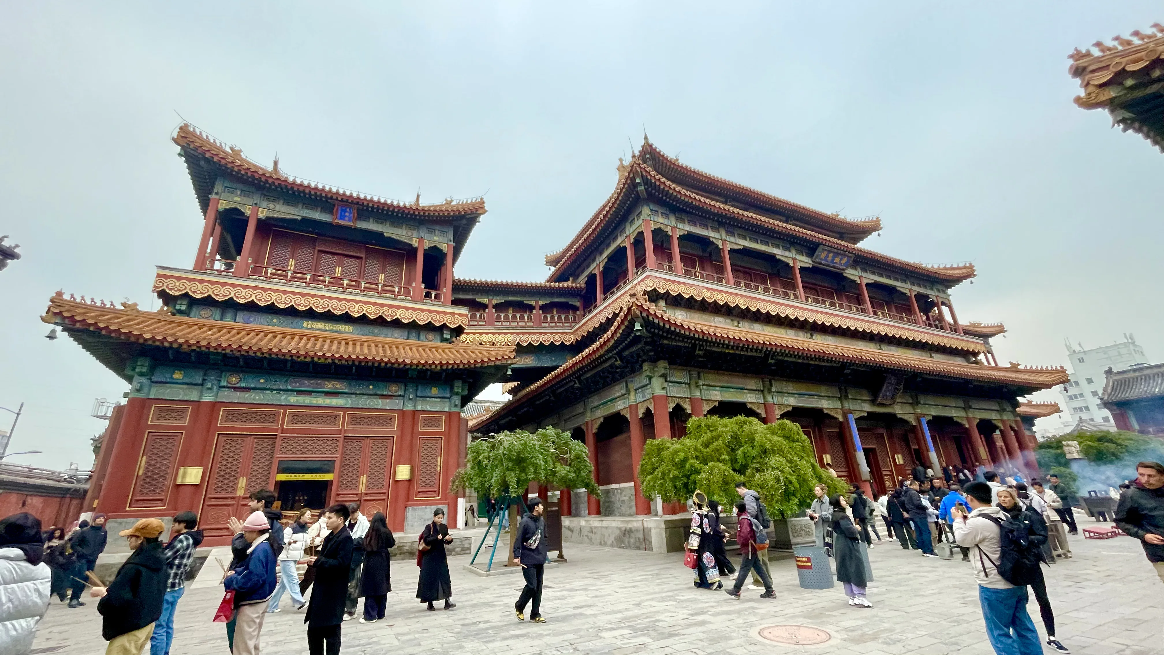 Pátio movimentado do Templo dos Lamas com edifícios tradicionais de arquitetura chinesa em tons de vermelho e dourado em Pequim.